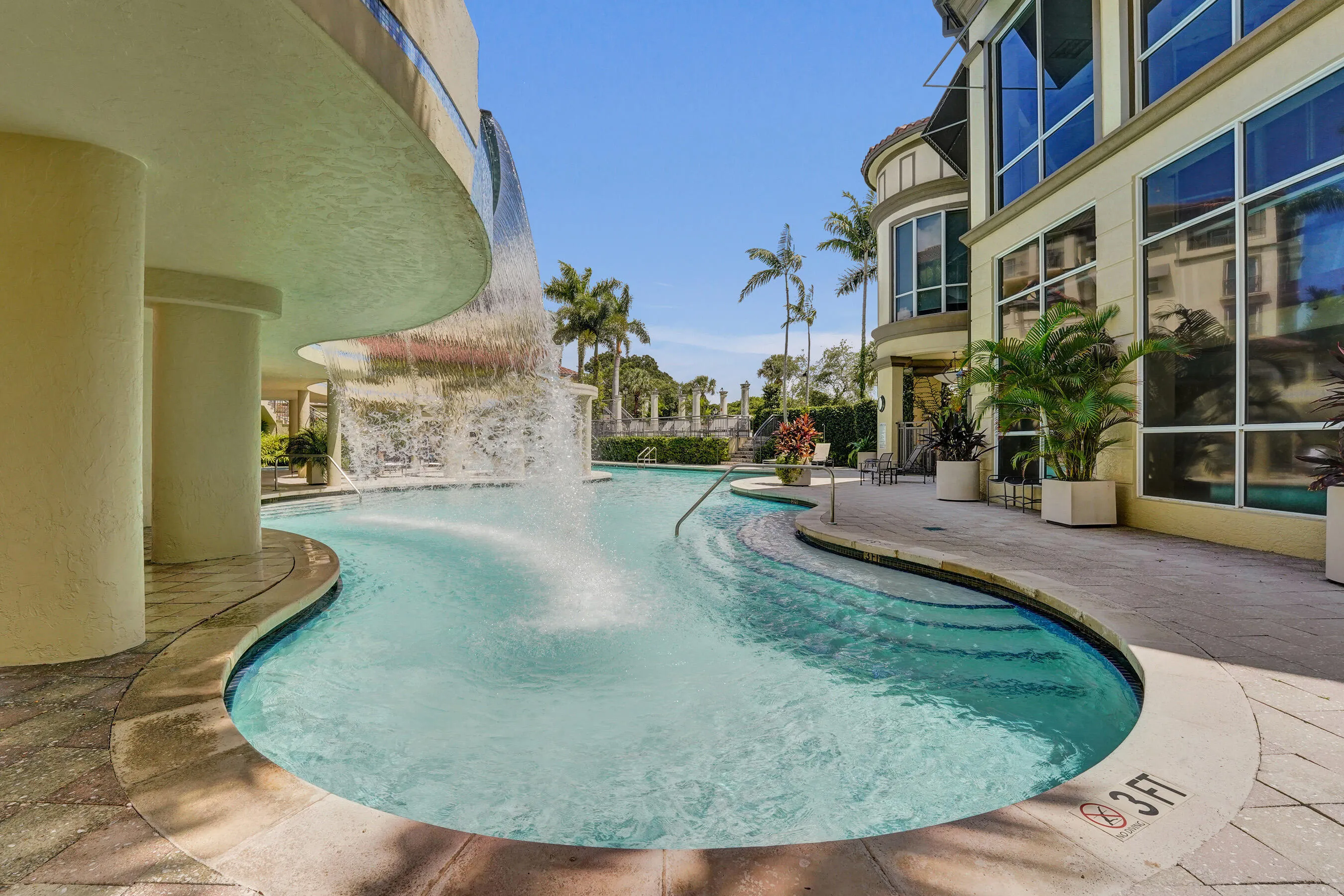 Resort-style pool with integrated waterfall feature, surrounding paved deck, and large pane windows