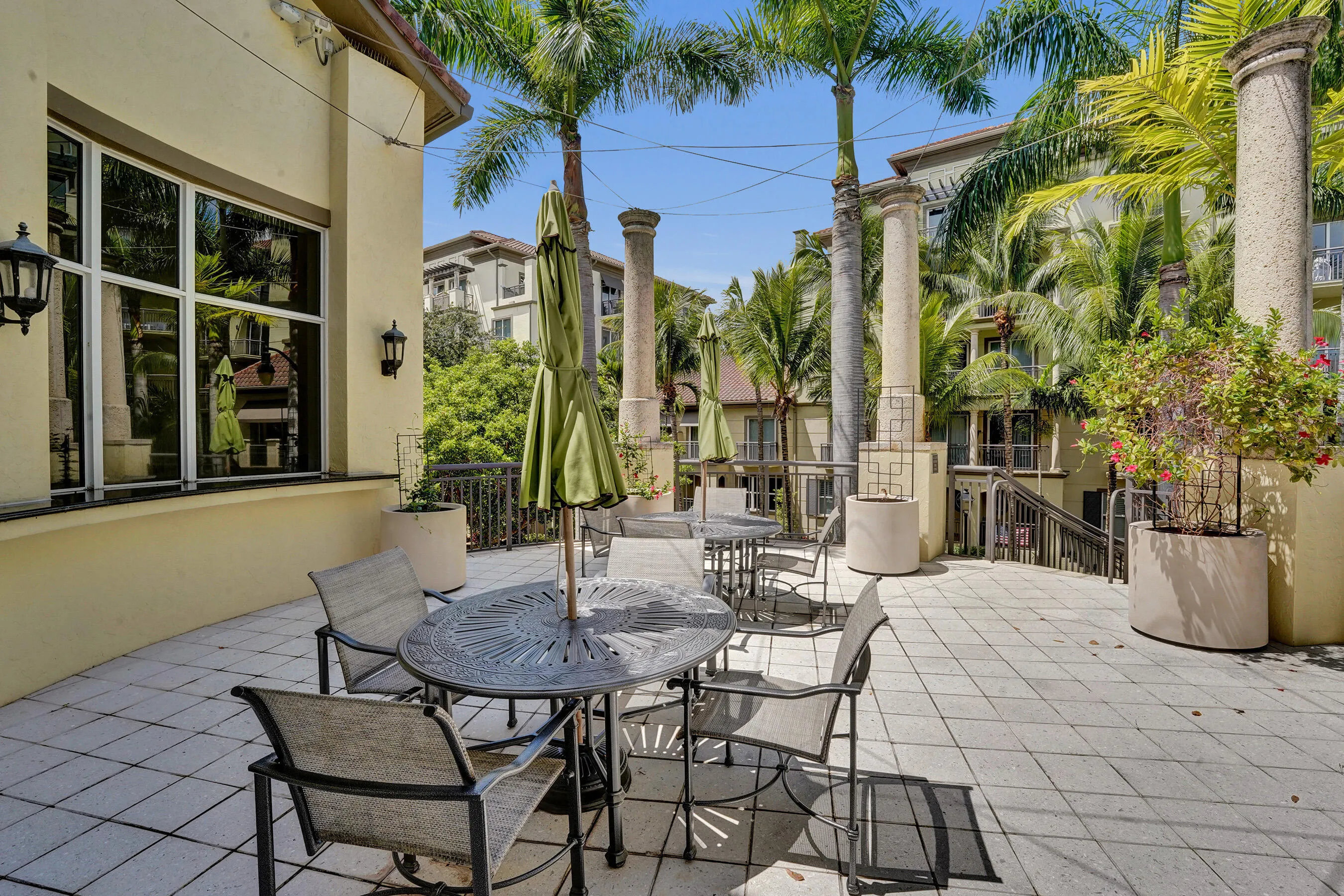 Expansive outdoor patio featuring paver flooring, architectural columns, wall-mounted exterior lighting, and mature palm trees