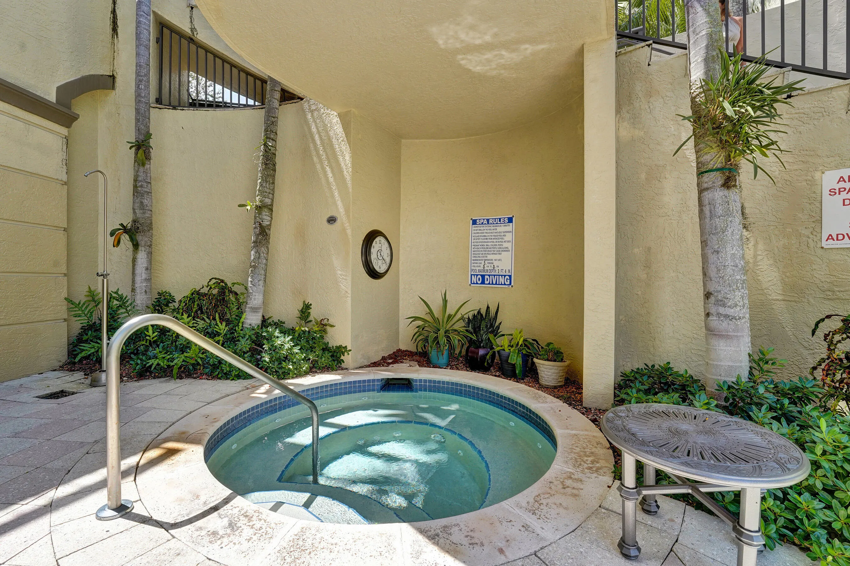 In-ground hot tub with integrated steps and a stainless steel handrail, surrounded by paver patio flooring and lush landscaping
