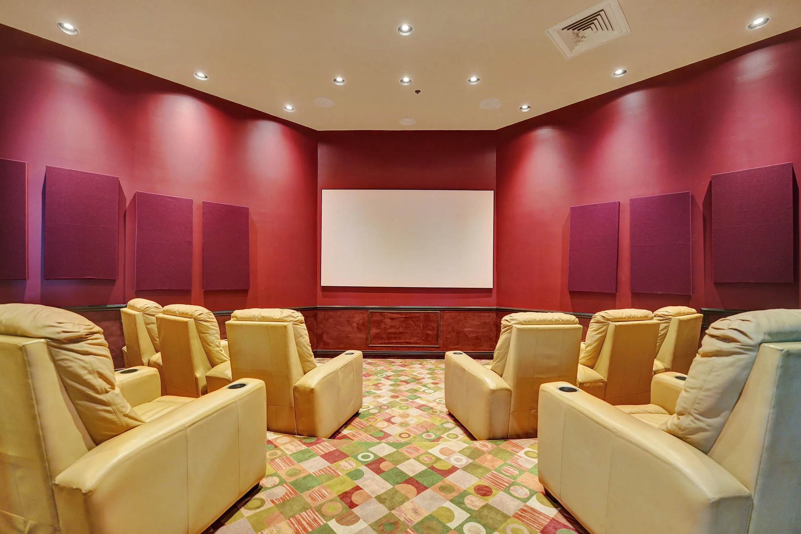 Dedicated media room with a large projection screen, recessed ceiling lighting, and wall-mounted sound panels