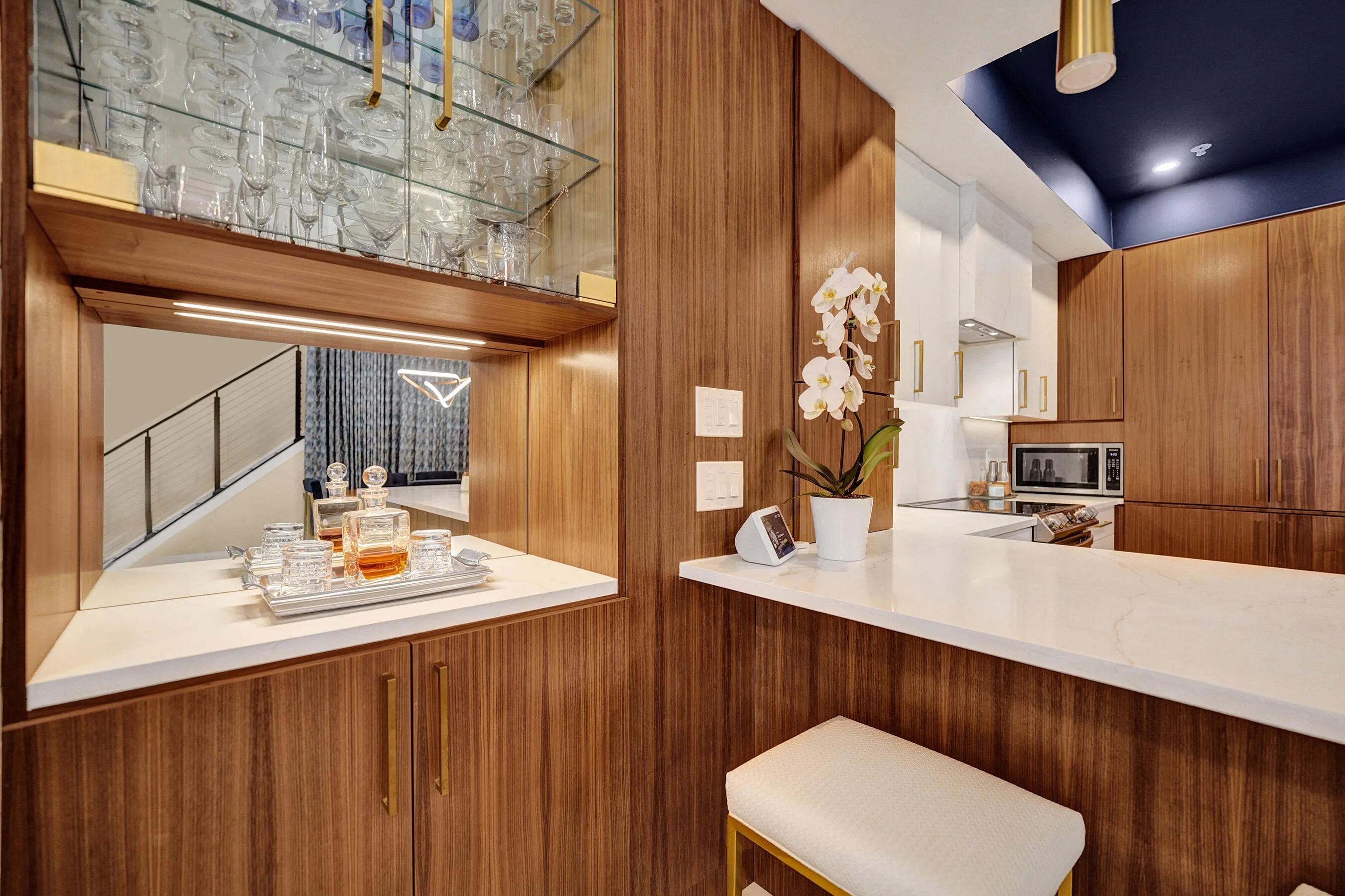 Built-in wet bar with mirrored backsplash and upper glass shelving, integrated kitchen featuring wood-finish cabinetry, white countertops, and a recessed ceiling with accent lighting