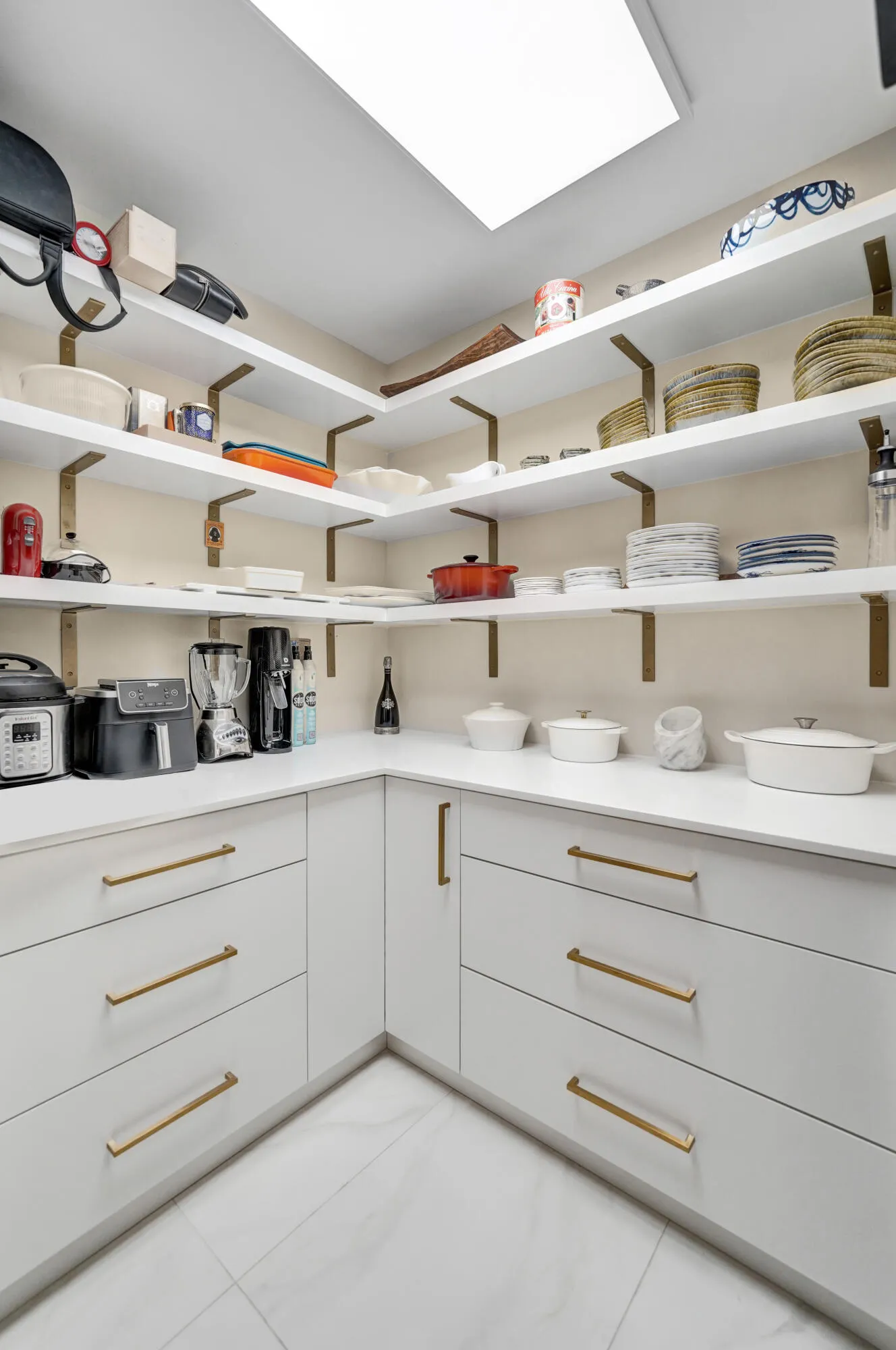 Built-in cabinetry with gold-tone hardware, white countertops, extensive open shelving with gold-tone brackets, and a recessed ceiling light