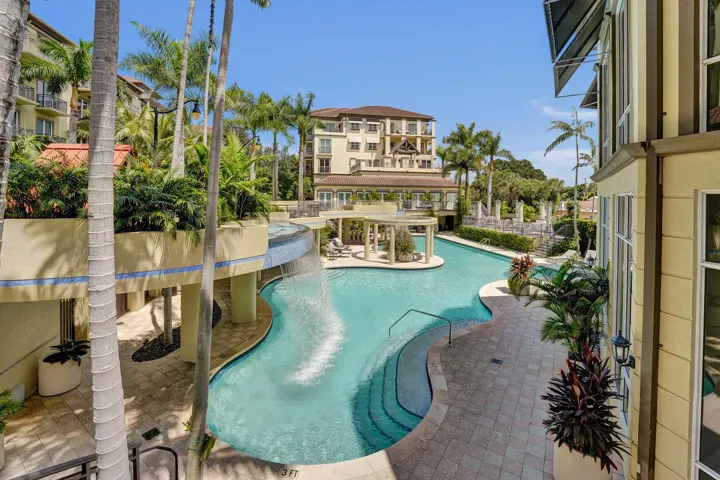Resort-style pool with a tiered waterfall feature, surrounded by mature palm trees and lush landscaping
