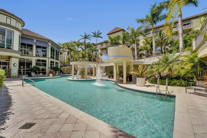 Resort-style pool with integrated waterfall feature, surrounding paved patio, and established tropical landscaping