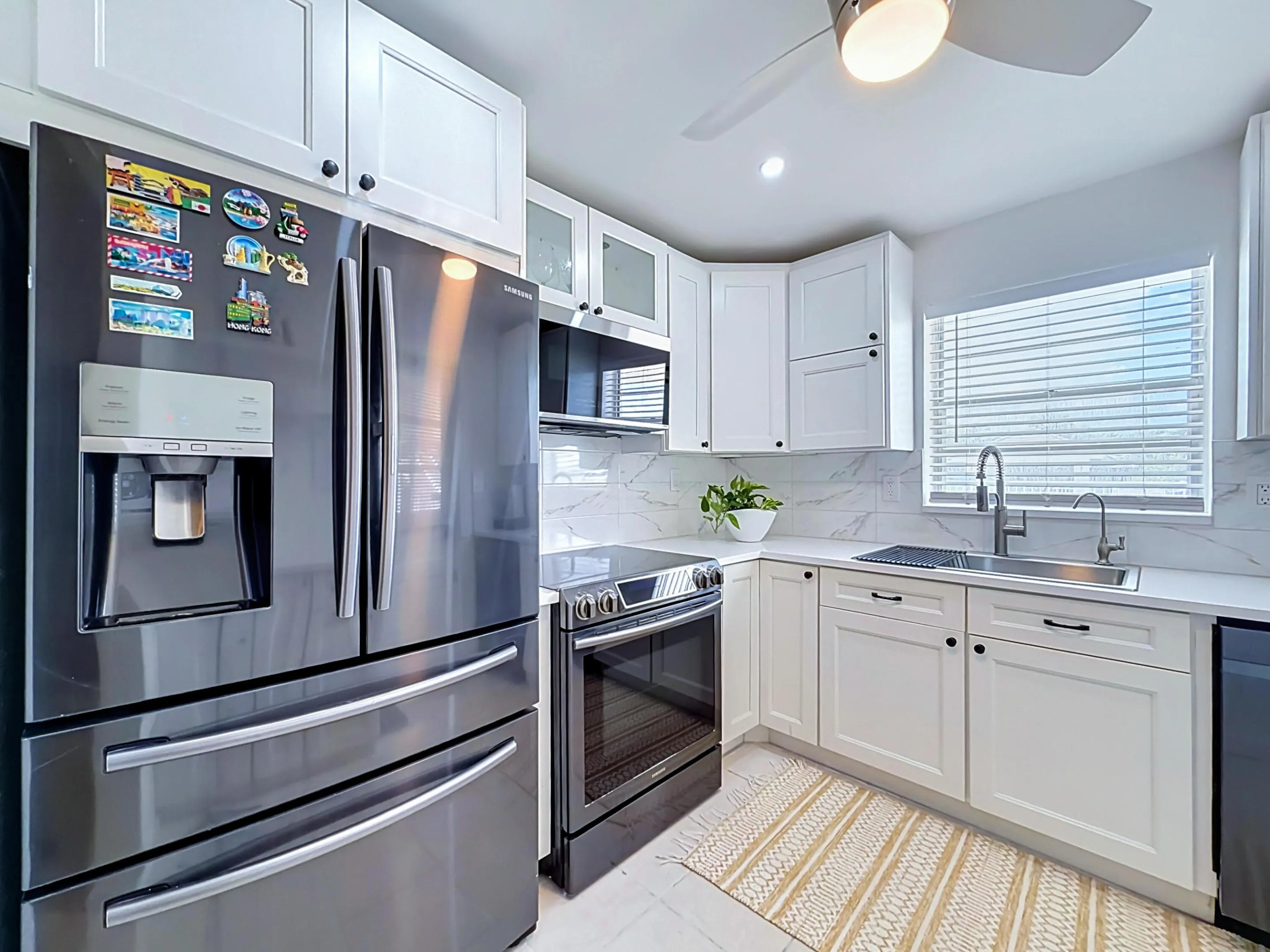 Kitchen featuring white shaker-style cabinetry, stainless steel appliances, a ceiling fan with integrated lighting, and a window with horizontal blinds