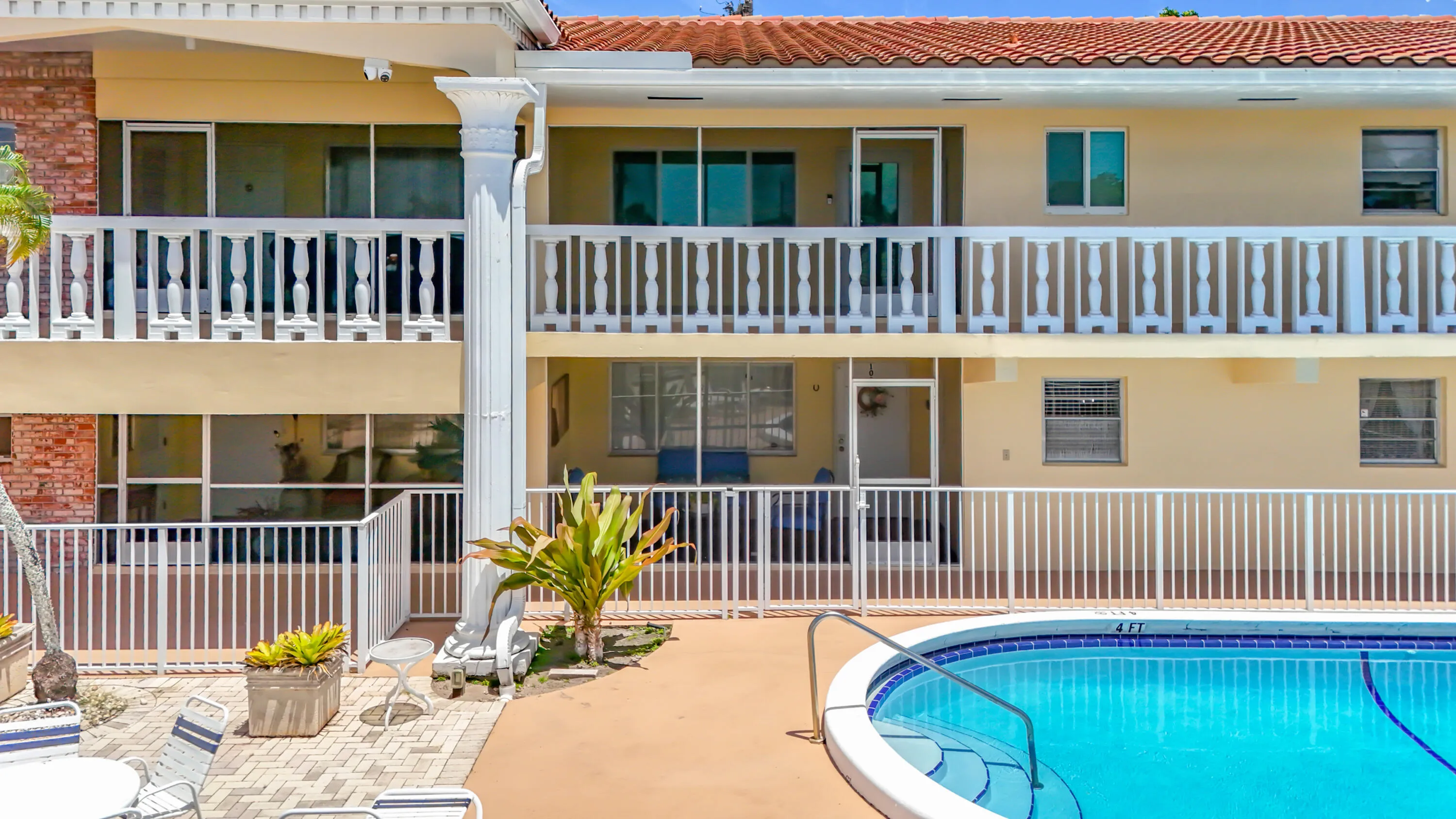 Arched swimming pool with tiled steps, surrounding paved patio, and white perimeter fencing