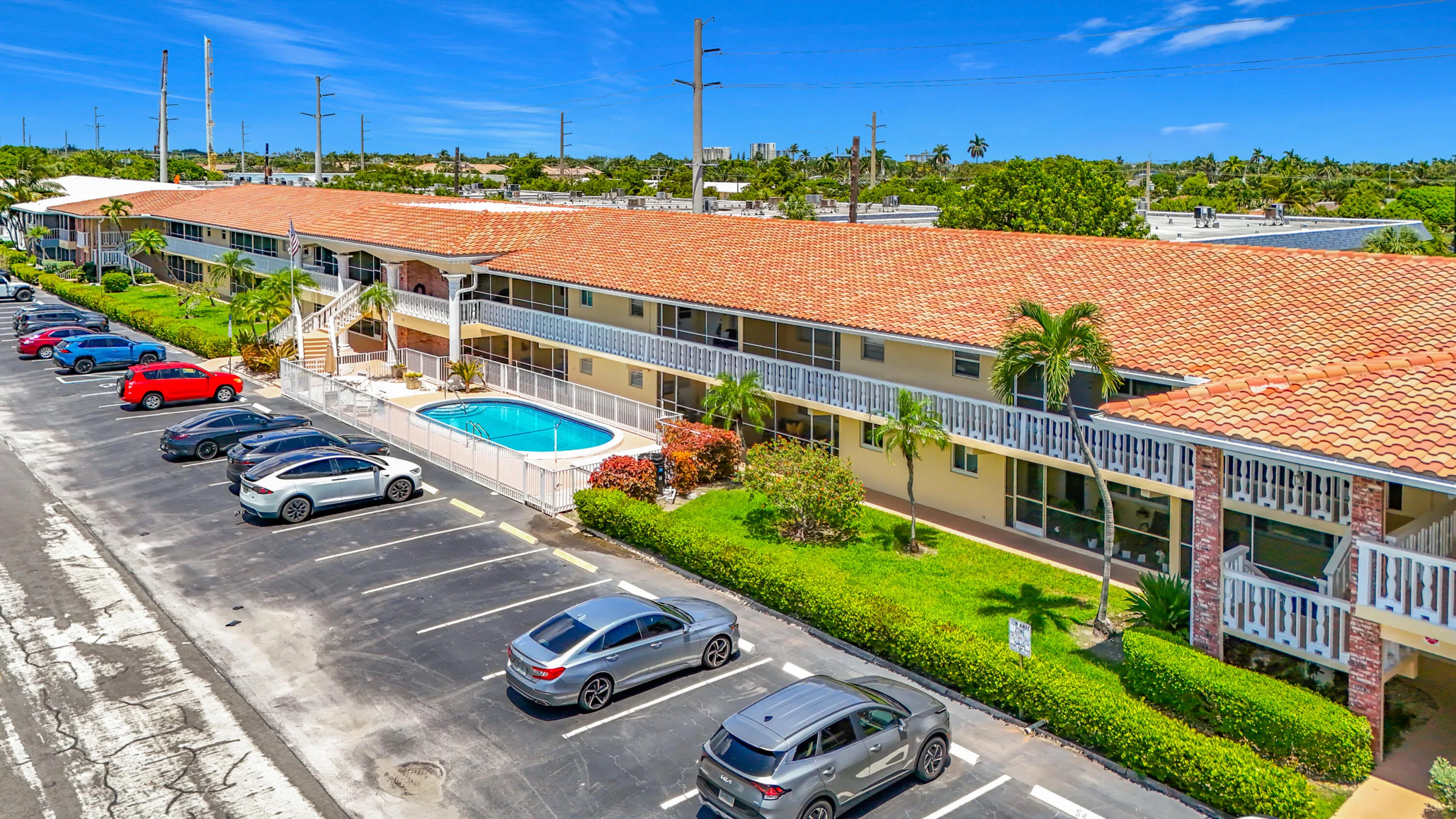 Multi-story building featuring terracotta tile roofing, a fenced swimming pool, and an asphalt parking area with marked spaces