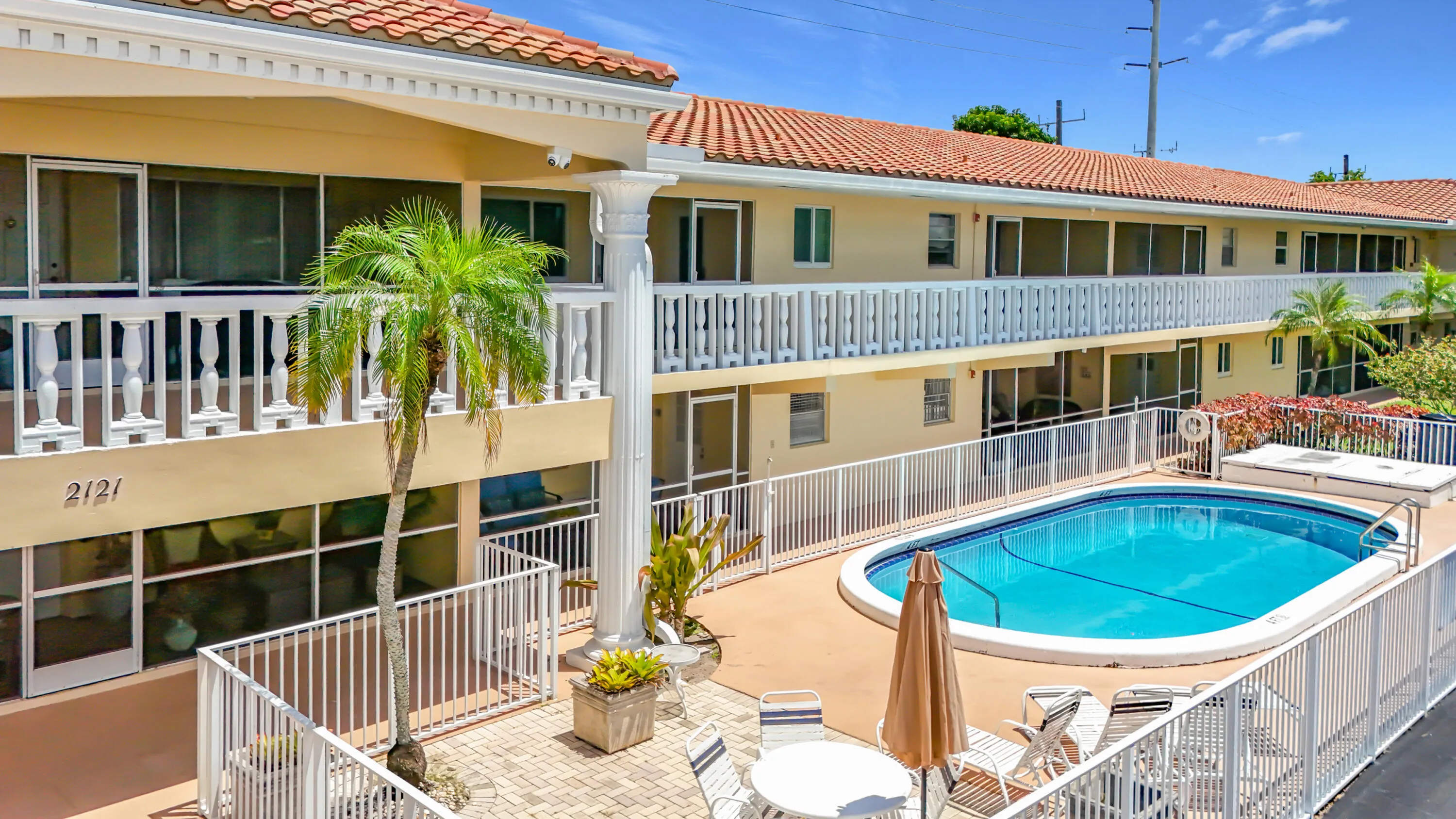 Building exterior with a red tile roof, white balustrade balconies, and a ground-level patio