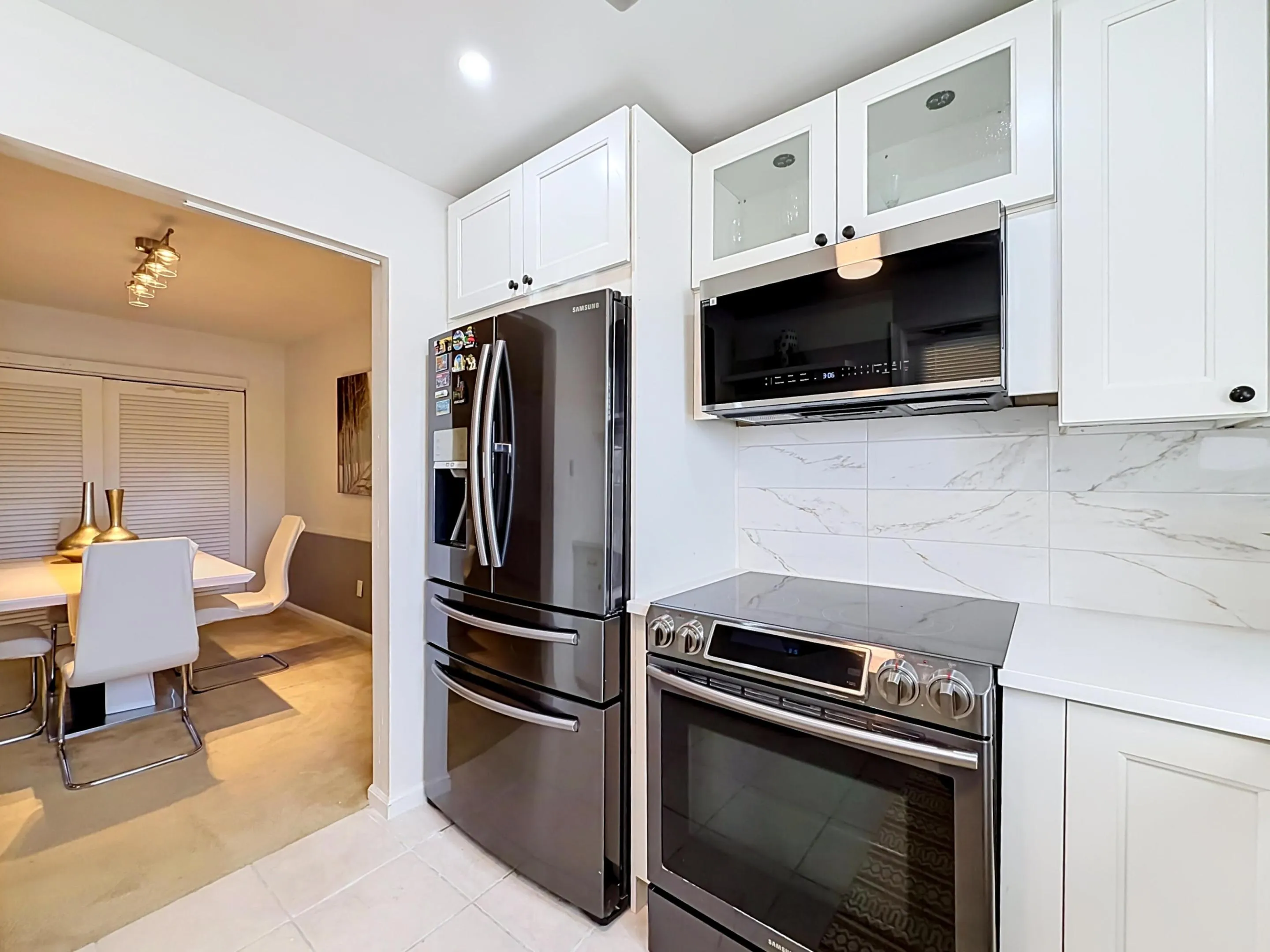White shaker cabinetry, modern dark stainless steel appliances, white quartz countertops, and a white marble-patterned tile backsplash