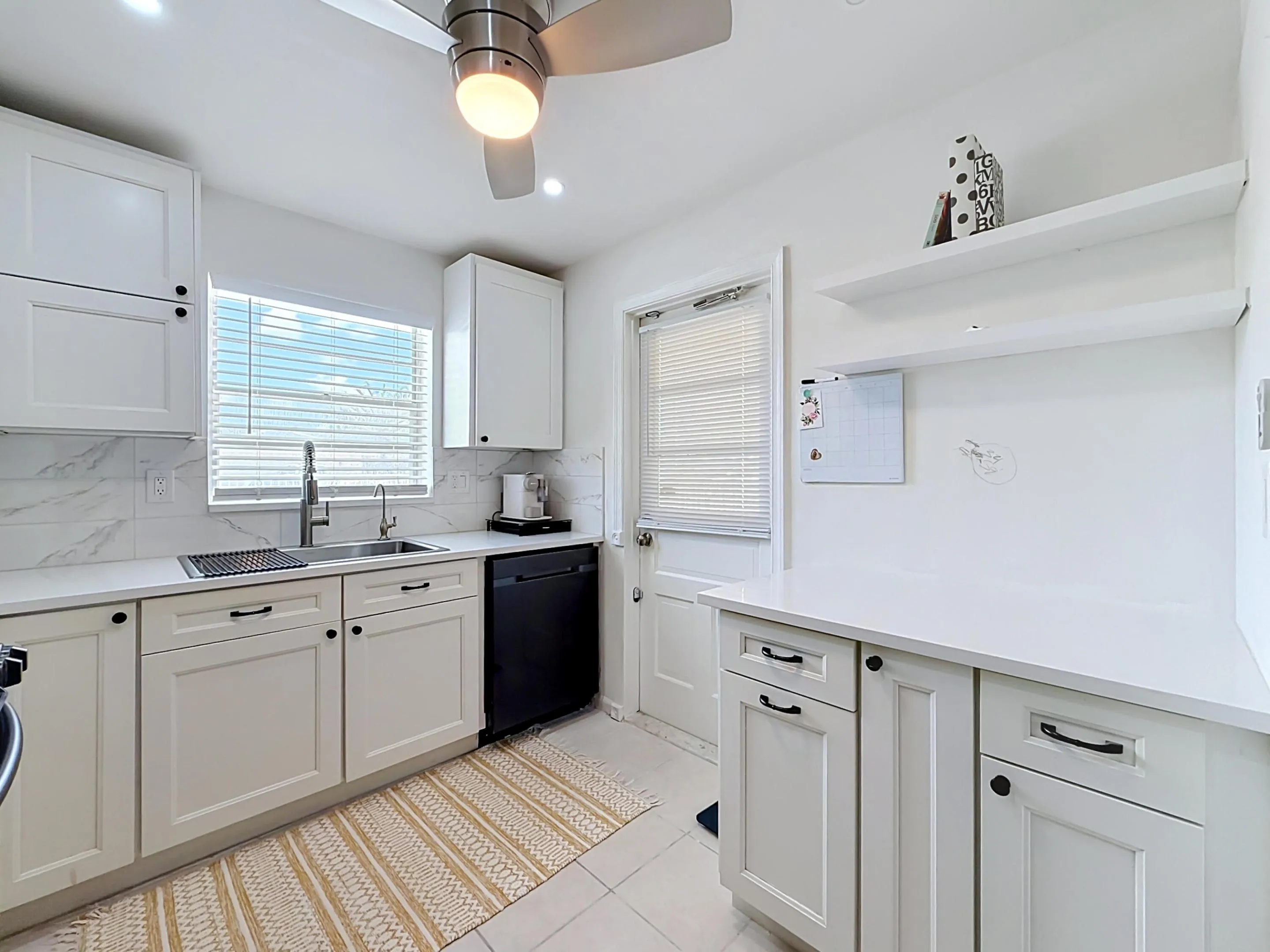 White cabinetry with matte black hardware, integrated dishwasher, stainless steel sink with gooseneck faucet, light-toned countertop, and tile backsplash