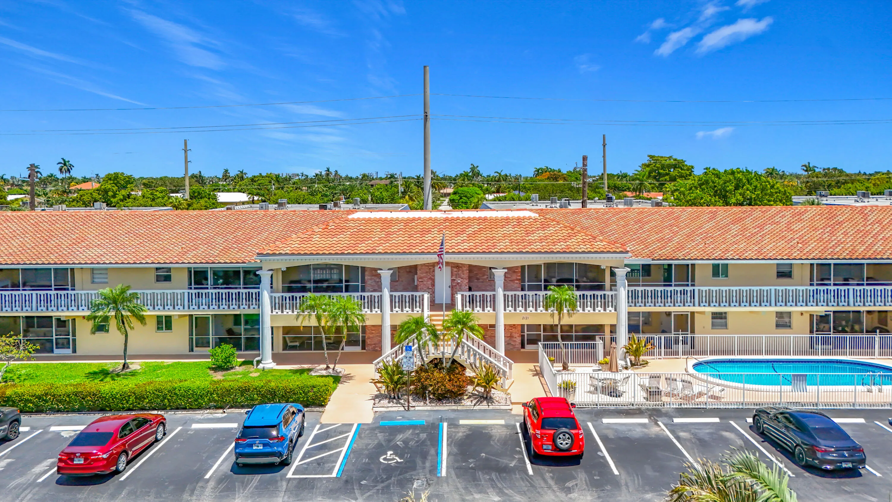 Multi-story building featuring a tile roof, multiple balconies, a swimming pool, and a paved parking area