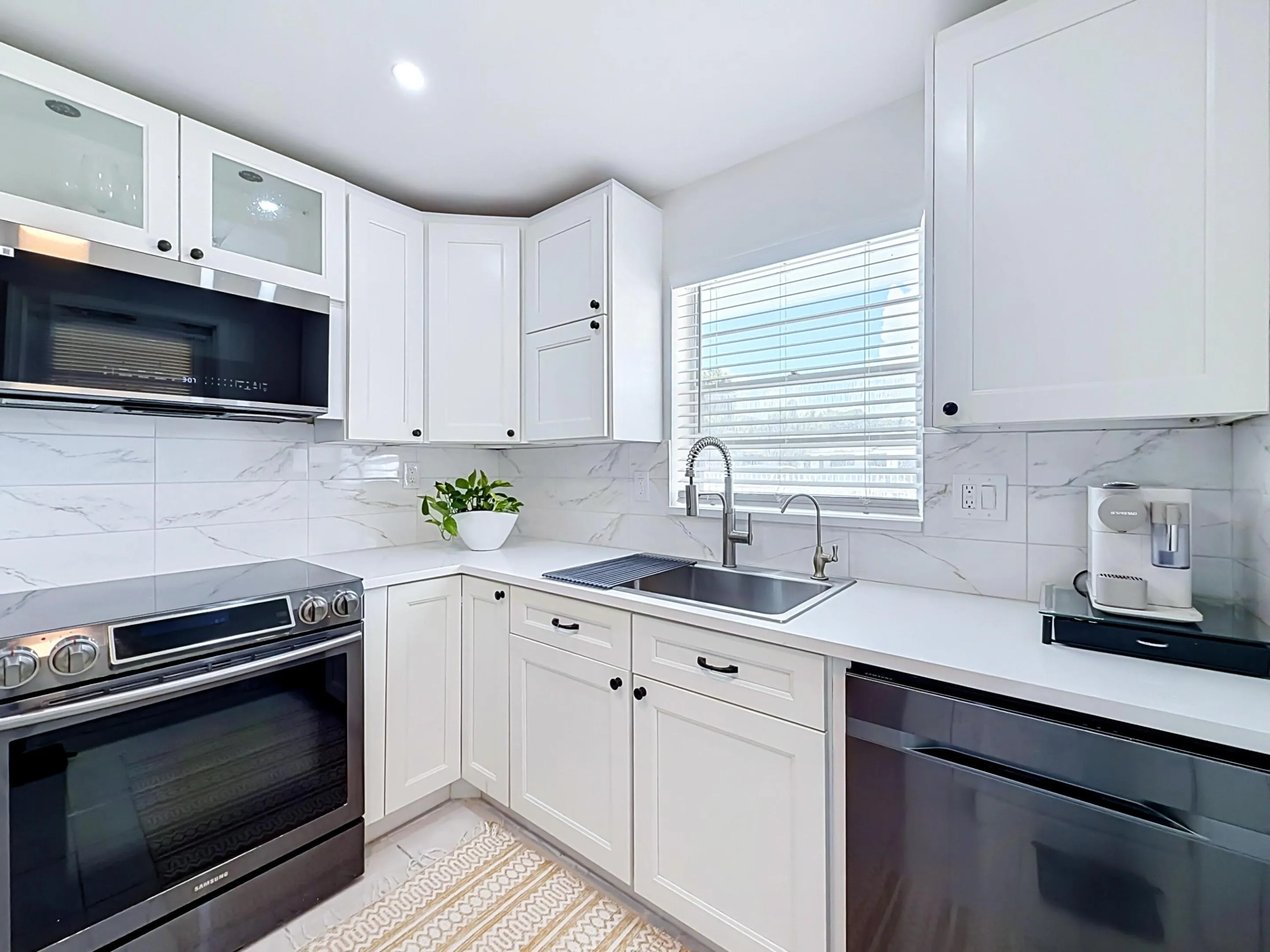 White shaker cabinetry, stone countertops, stainless steel sink with gooseneck faucet, black oven range, and coordinating black dishwasher