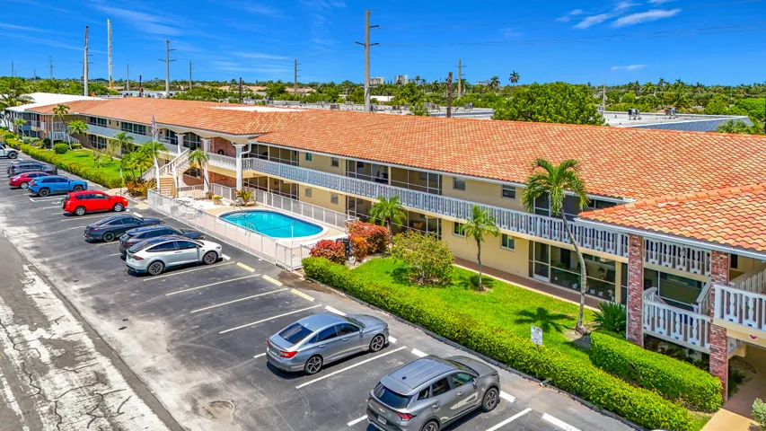 Multi-story building featuring terracotta tile roofing, a fenced swimming pool, and an asphalt parking area with marked spaces