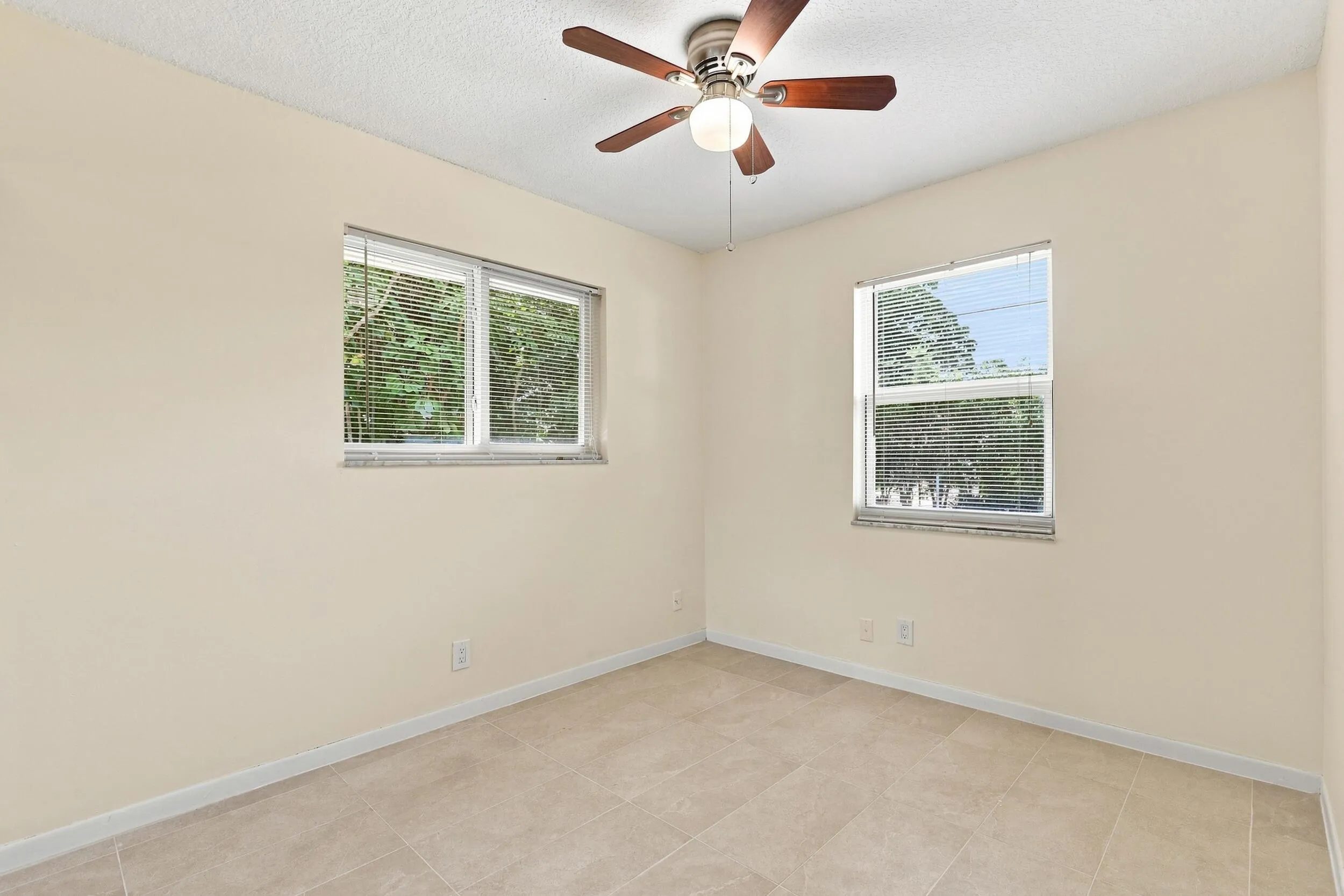Bright bedroom with ceiling fan, neutral finishes, and multiple windows.