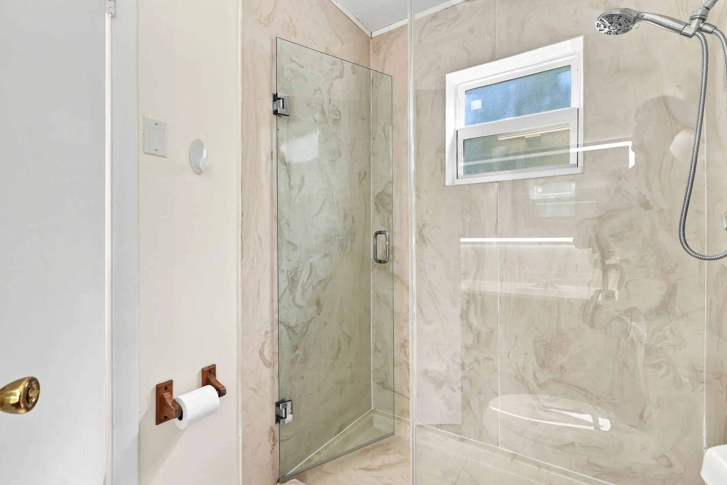 Updated shower featuring glass doors, tiled walls, and a window for natural light.