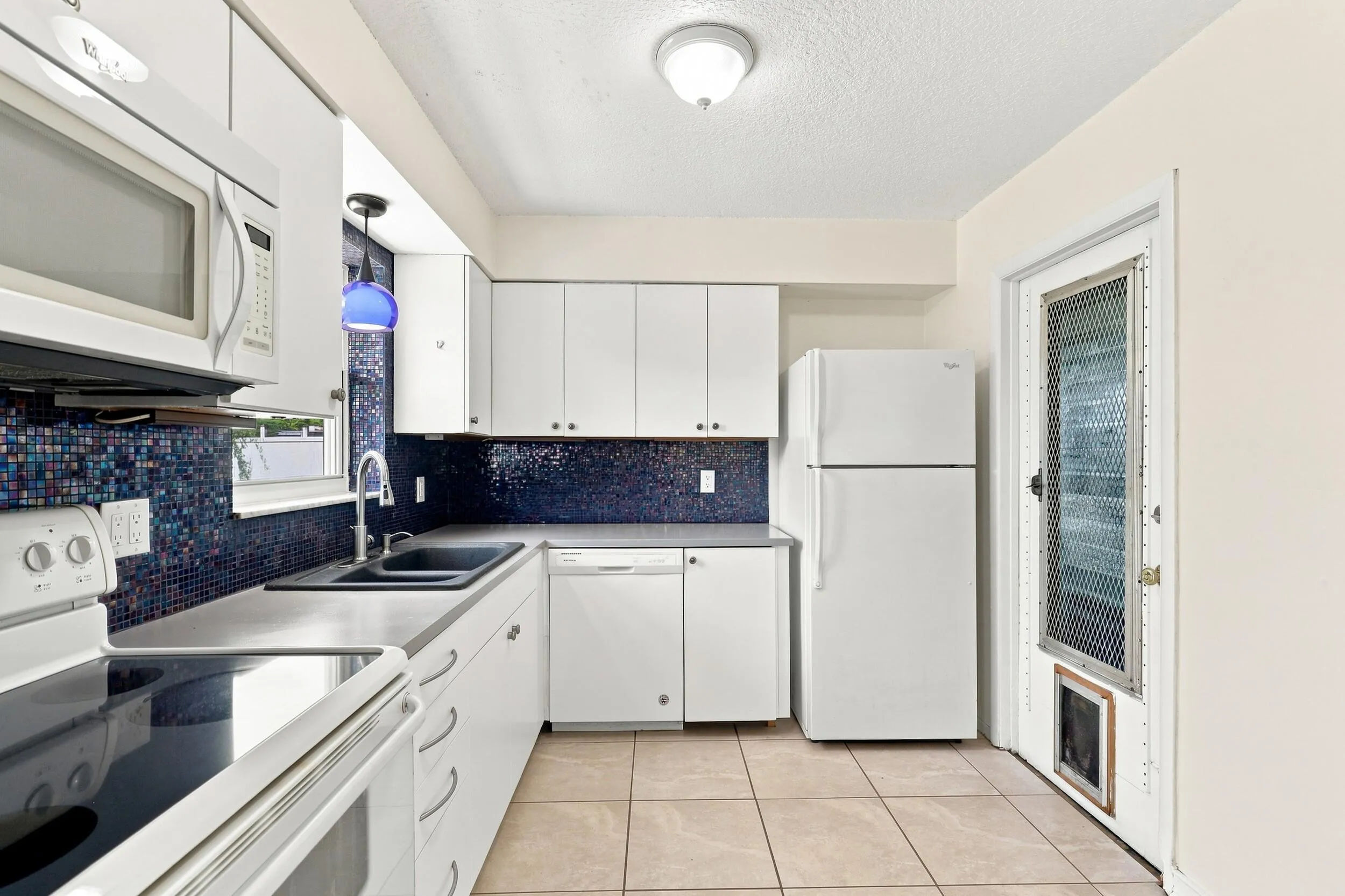 Functional kitchen with white cabinetry, generous storage, and access to the exterior.