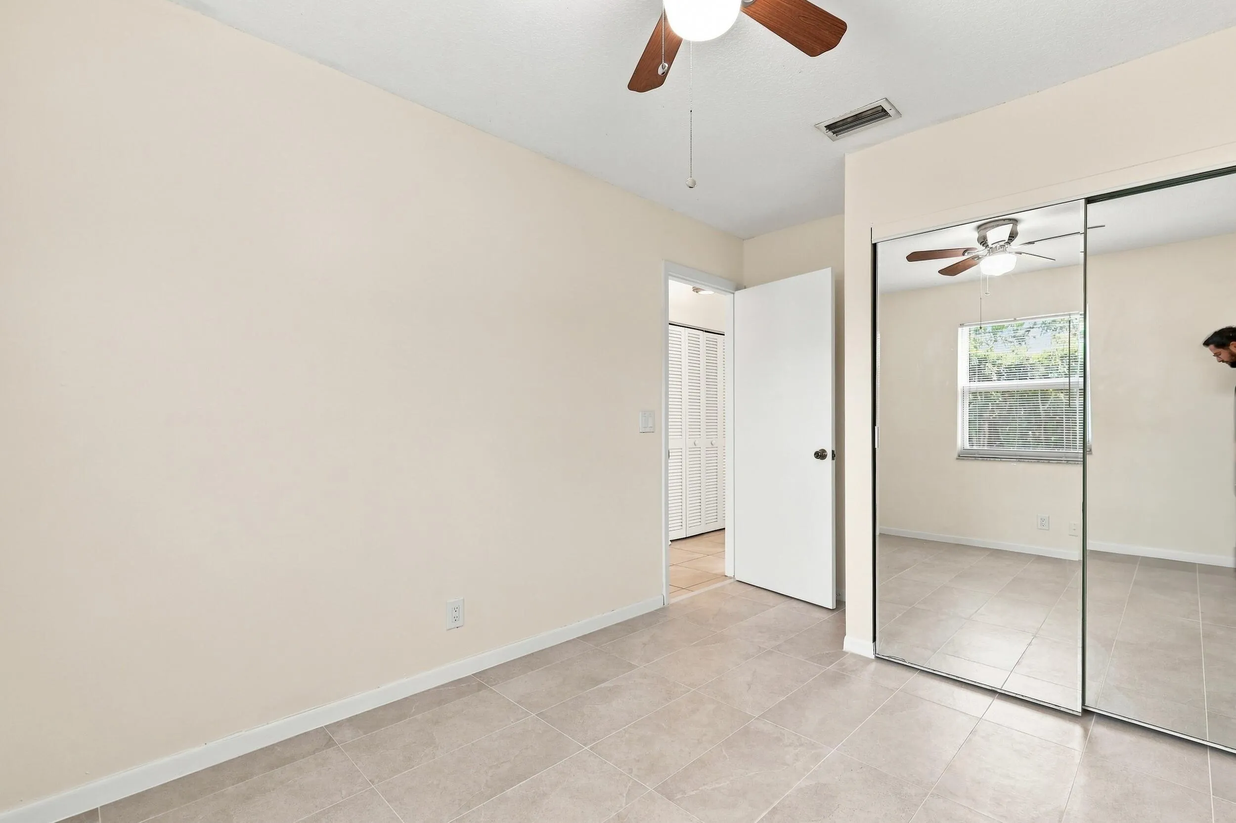 Bedroom featuring a ceiling fan, neutral flooring, and mirrored closet doors.