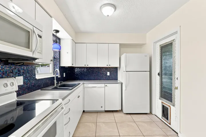 Functional kitchen with white cabinetry, generous storage, and access to the exterior.