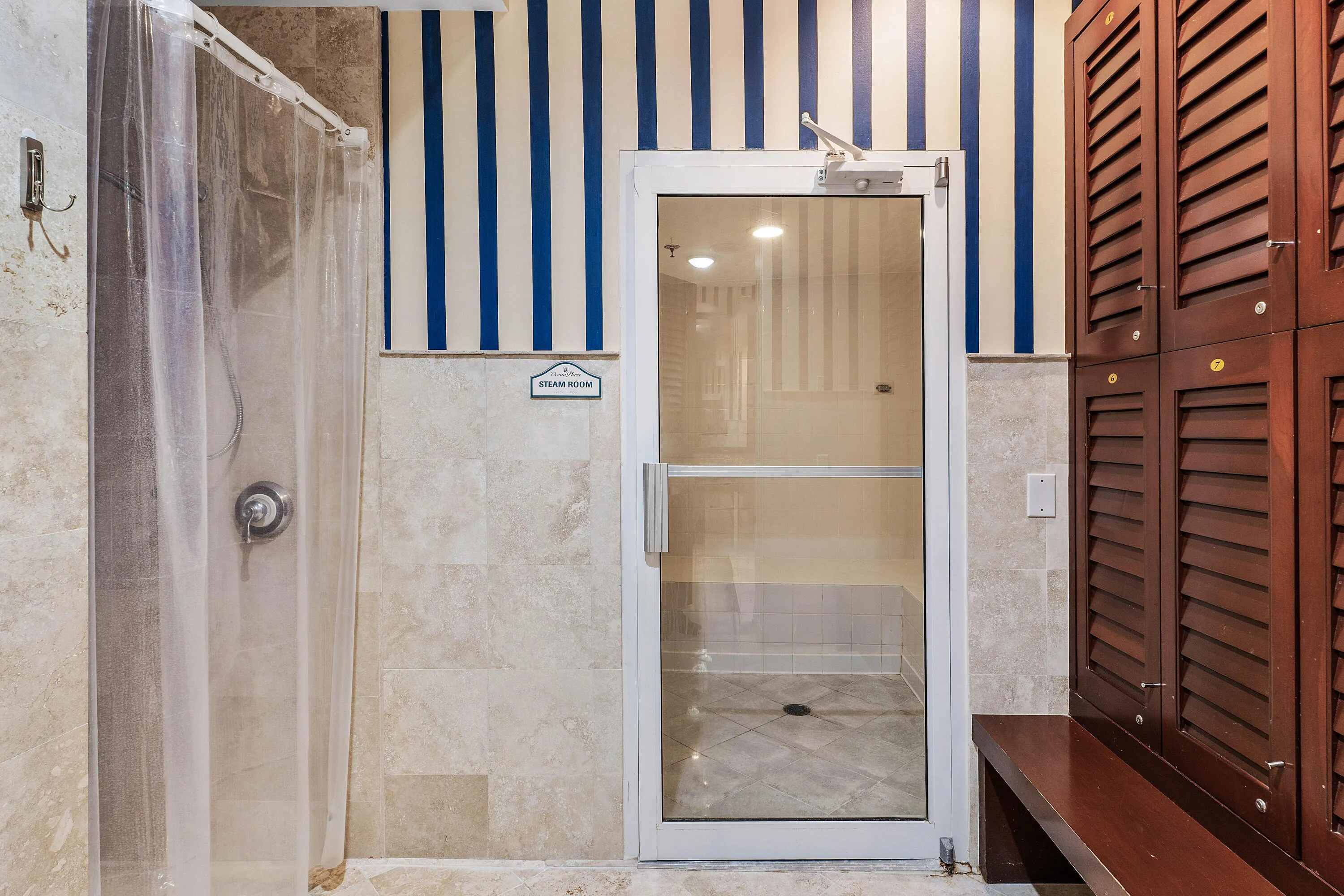 Tiled shower area with a chrome fixture, full glass door entry, and wood-finish locker storage