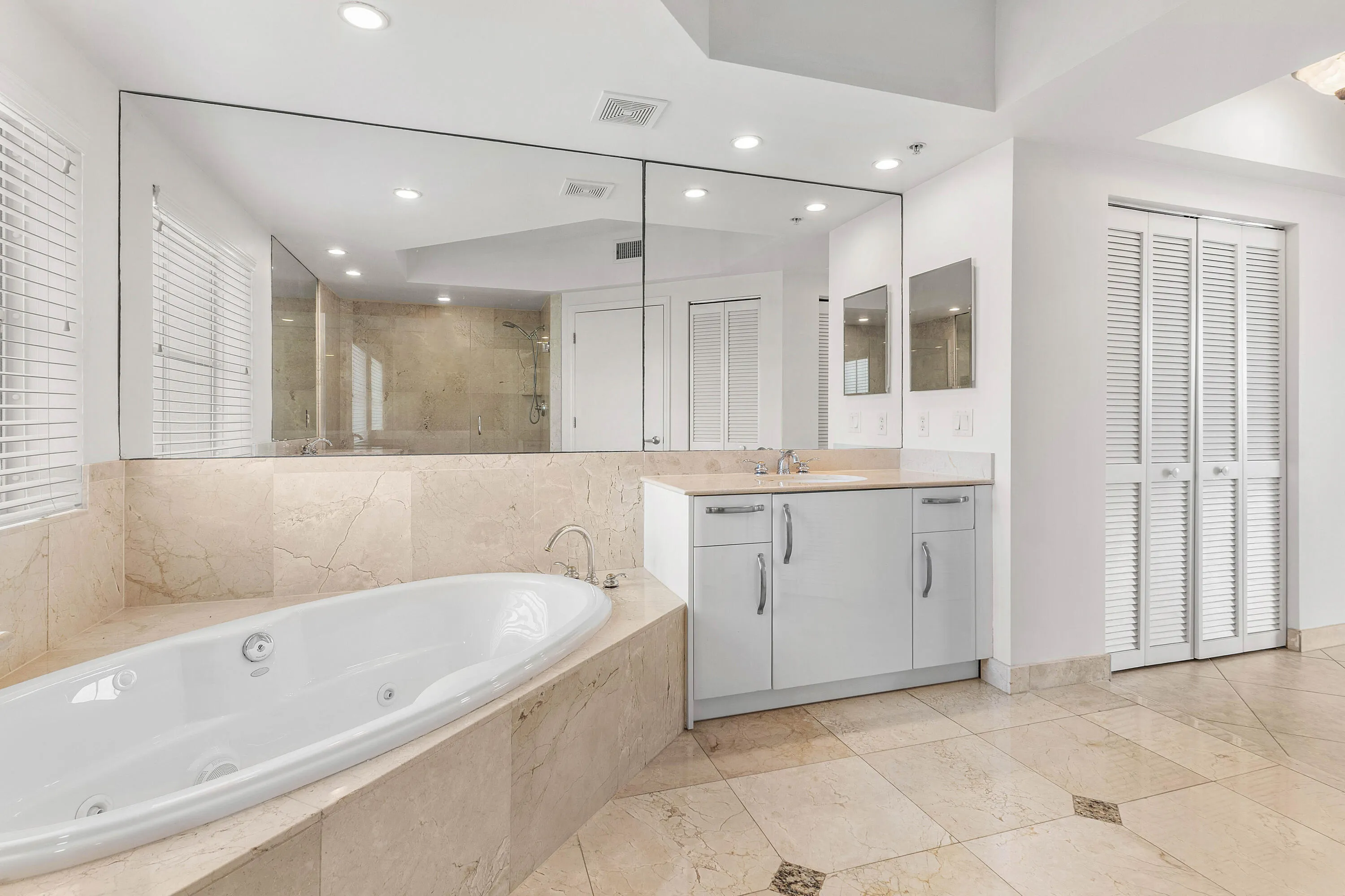 Soaking tub with a tiled surround, dual-sink vanity, full-width mirror, and louvered bifold doors