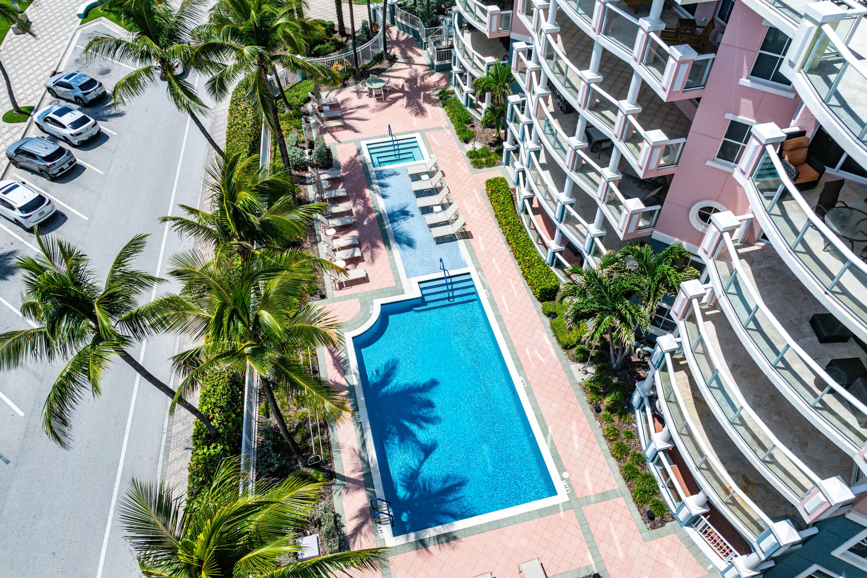 Resort-style swimming pool with sun lounging area, surrounded by mature palm landscaping and multi-story residential buildings with contemporary architecture and balconies