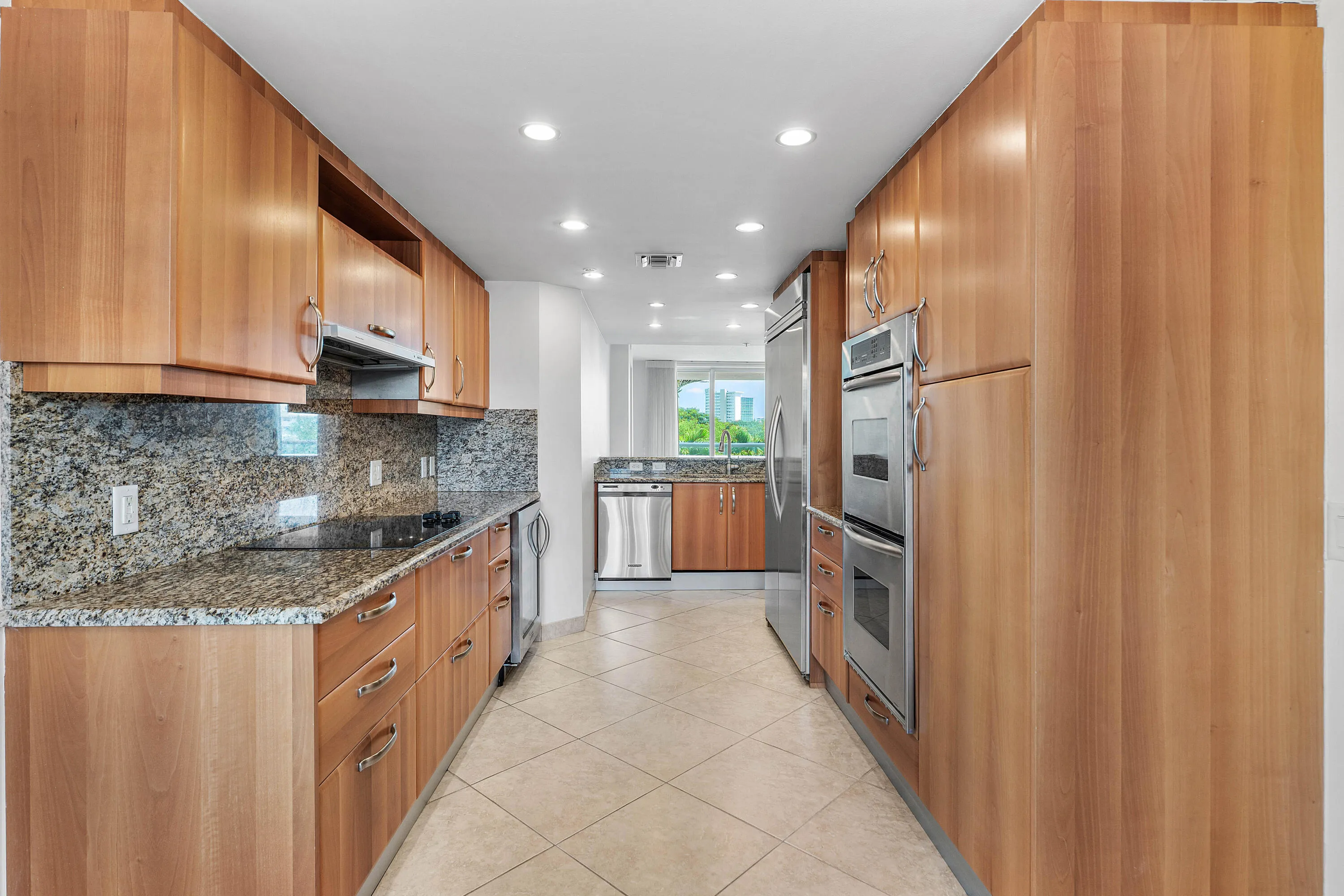 Galley kitchen featuring wood cabinetry, granite countertops, tile flooring, and integrated stainless steel appliances including double ovens.