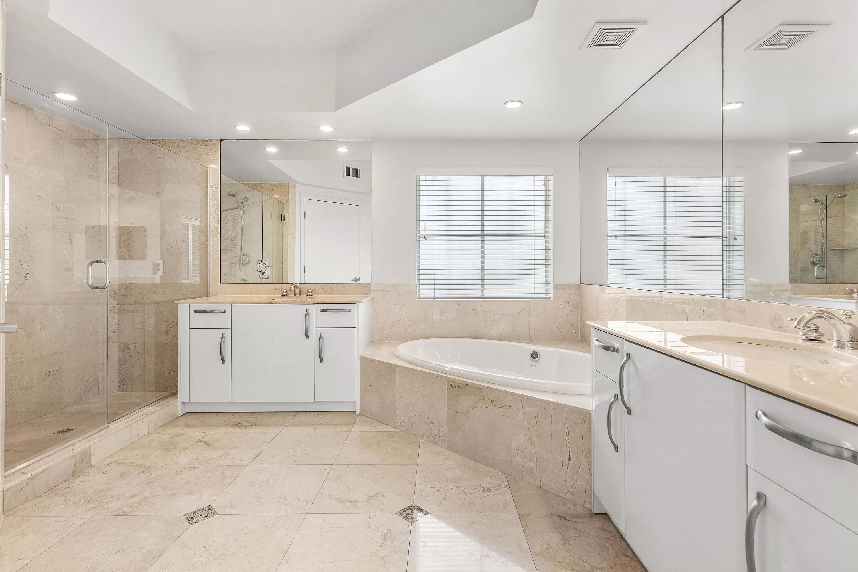 Tiled flooring with accent details, dual vanity with undermount sinks, built-in soaking tub, glass-enclosed shower, and expansive wall-mounted mirrors