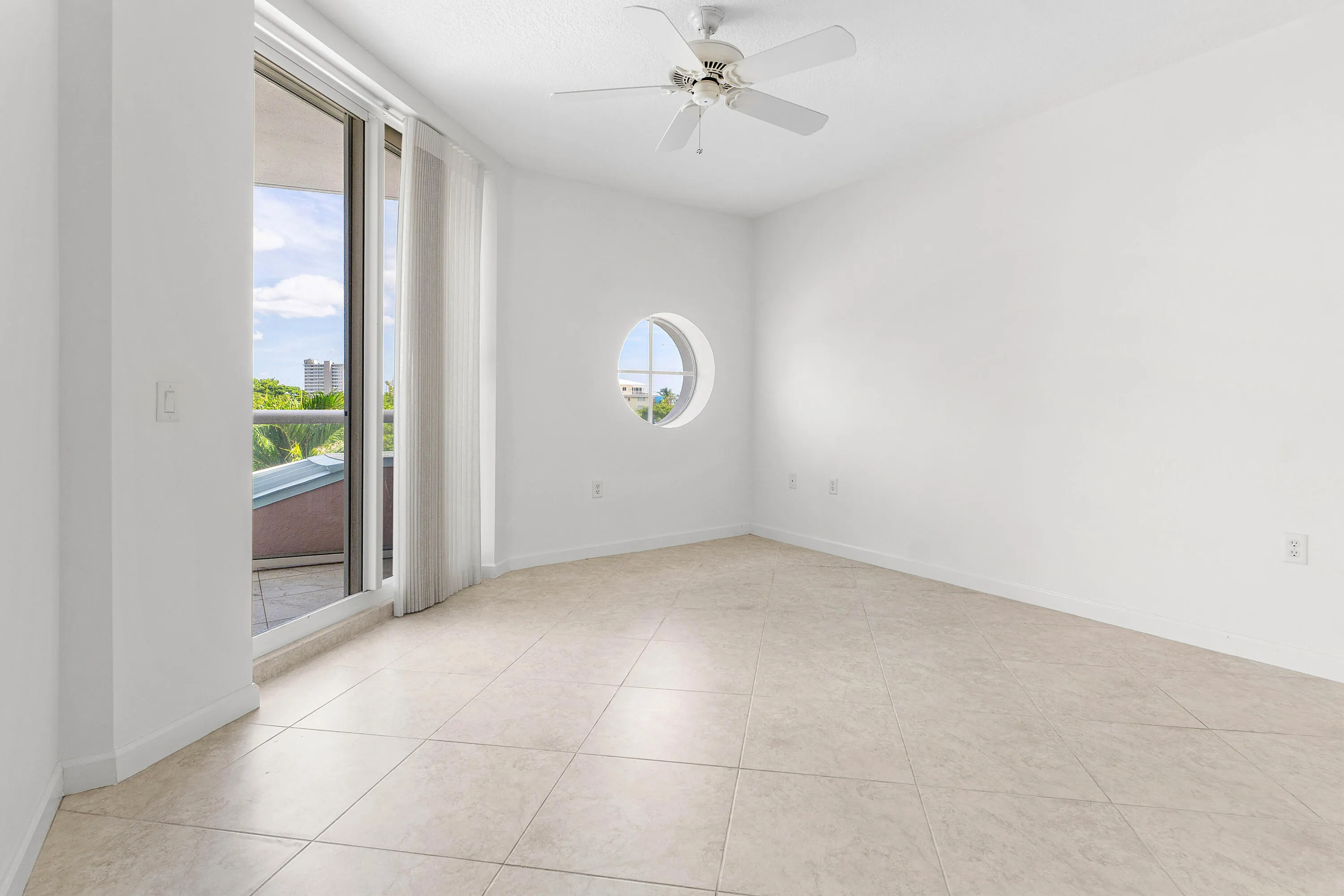 Neutral-toned tile flooring, round porthole window, glass sliding doors, private balcony, and a ceiling fan