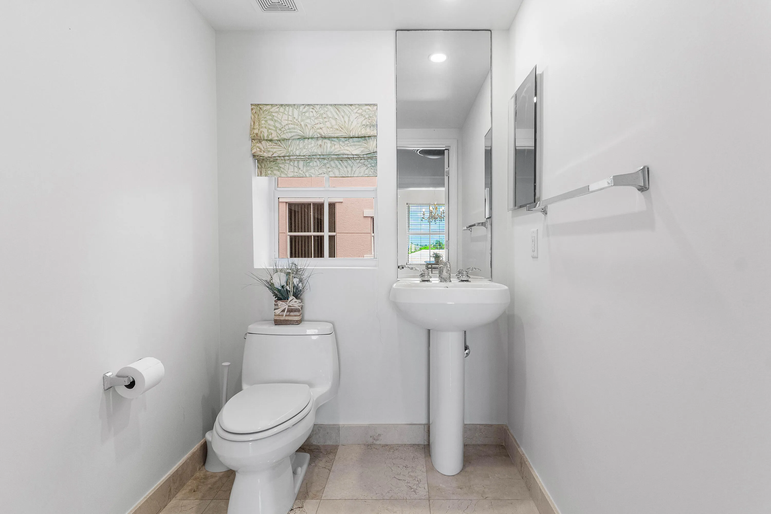 White pedestal sink with chrome faucet, full-length wall mirror, and neutral-toned tile flooring