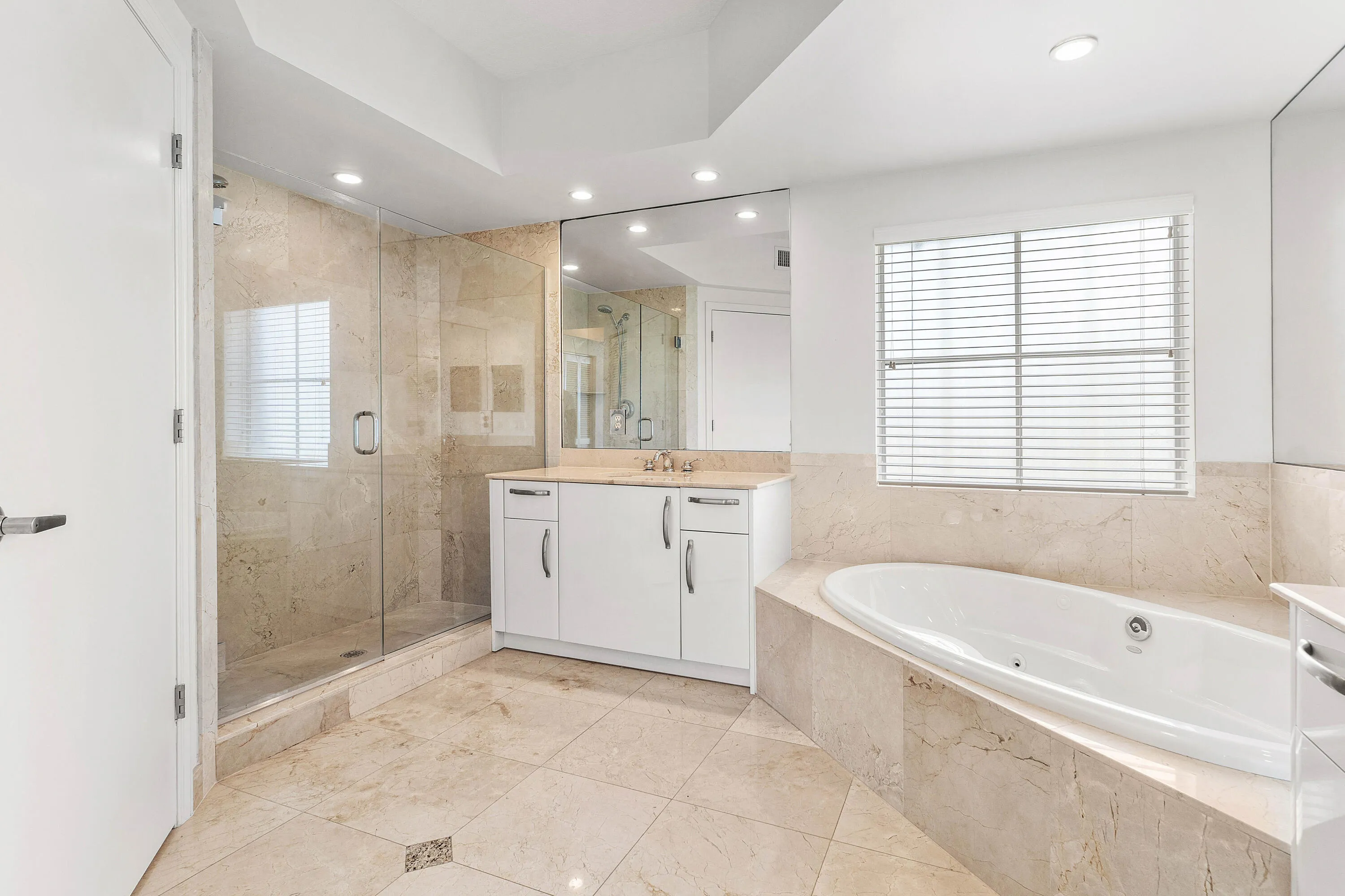 Tiled flooring with accent details, dual vanity with undermount sinks, built-in soaking tub, glass-enclosed shower, and expansive wall-mounted mirrors