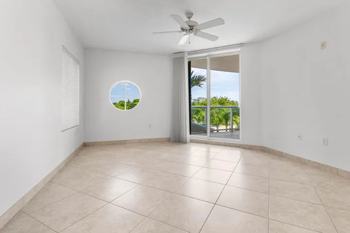 Neutral-toned tile flooring, white walls, ceiling fan, circular window, and sliding glass door to a balcony