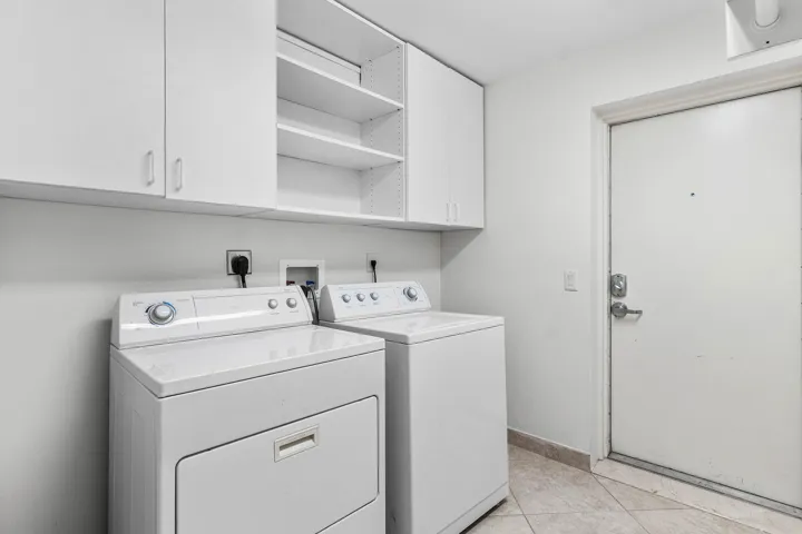 Dedicated laundry area featuring white upper cabinetry, open shelving, and light-toned tile flooring