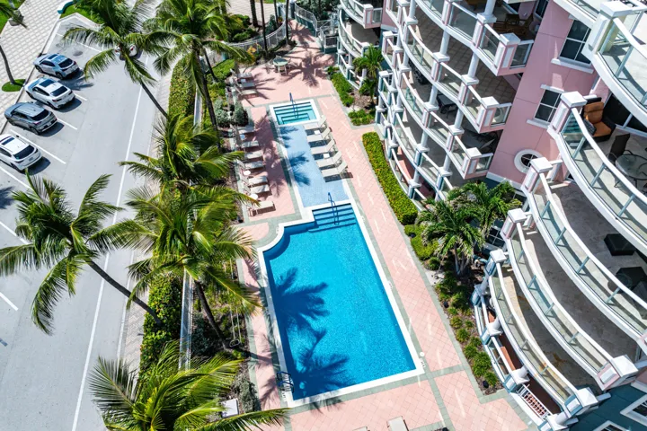 Resort-style swimming pool with sun lounging area, surrounded by mature palm landscaping and multi-story residential buildings with contemporary architecture and balconies