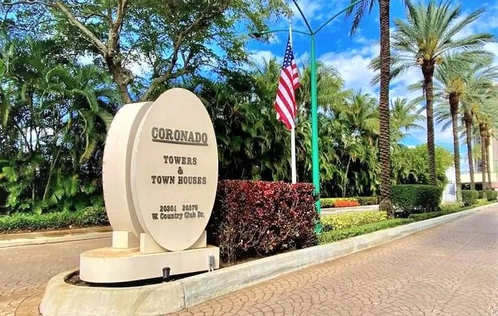 Entrance sign for Coronado Towers & Town Houses, surrounded by lush landscaping, mature palm trees, and a paved driveway