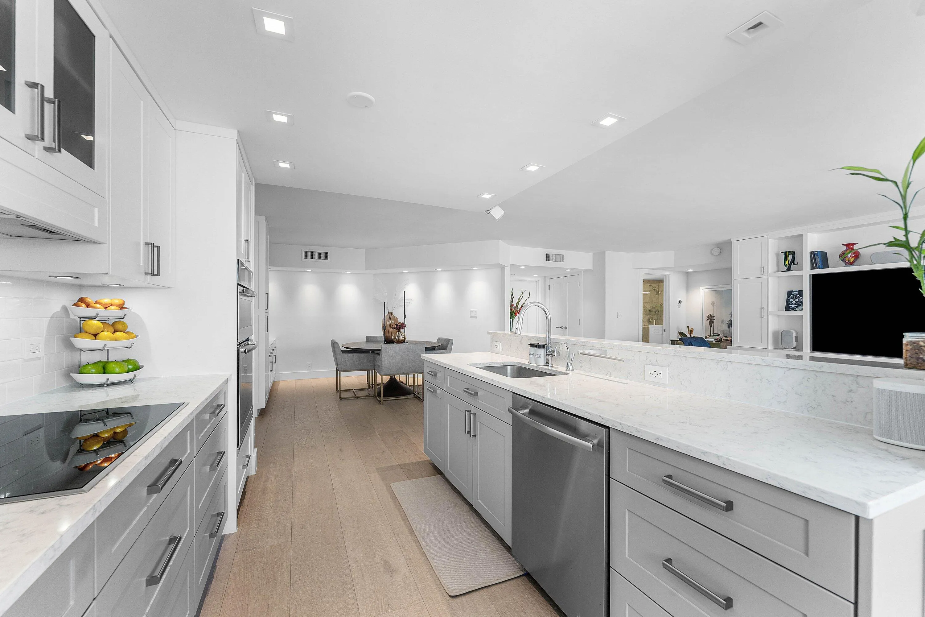 Contemporary kitchen featuring light wood-finish flooring, white cabinetry, gray lower cabinetry, integrated stainless steel appliances, and white countertops