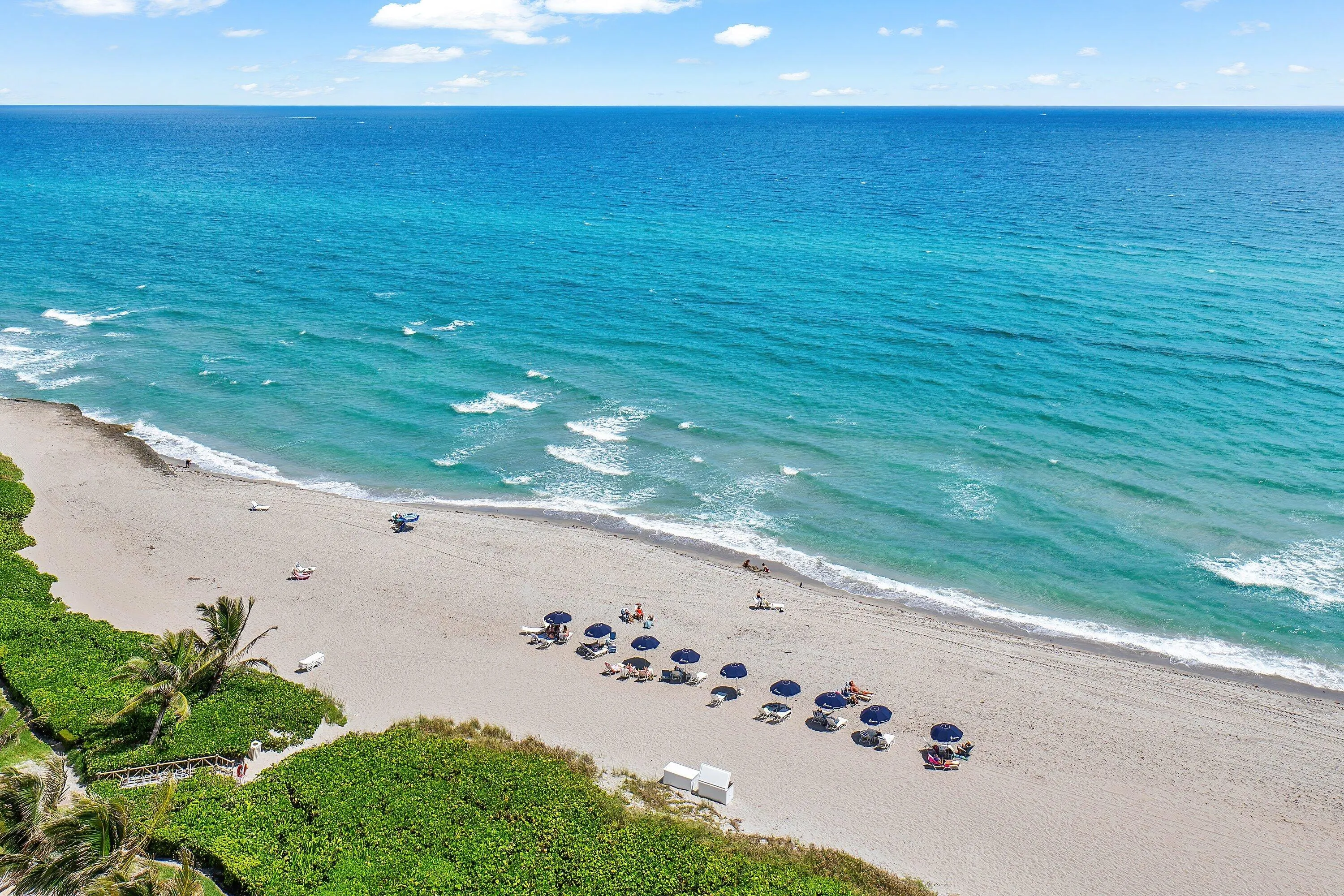 Expansive beachfront with direct ocean access, featuring a wide sandy beach, clear blue water, and lush tropical landscaping