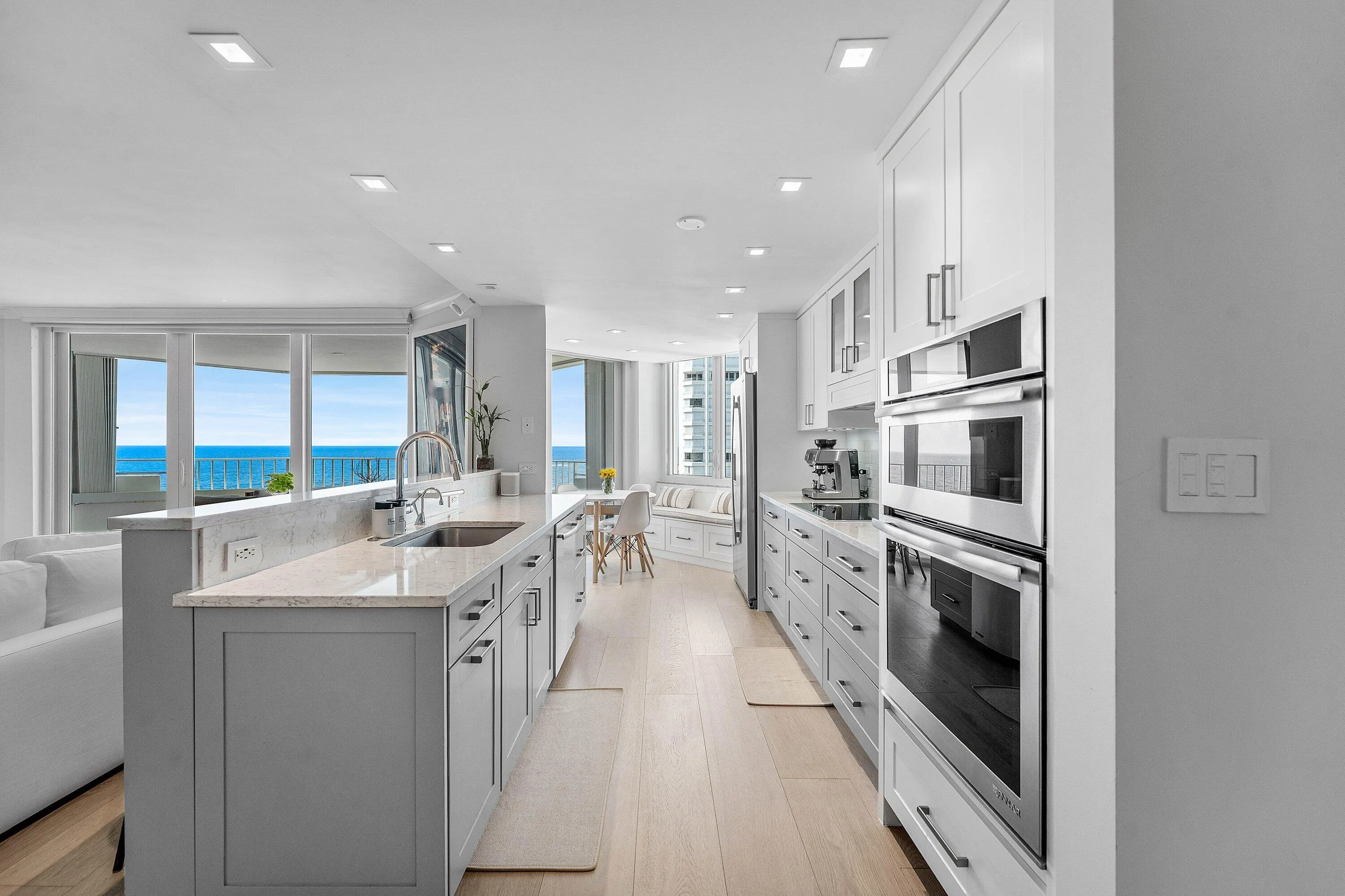 Galley kitchen with light wood-finish flooring, two-tone cabinetry, stainless steel appliances, recessed lighting, and a window with water visible beyond