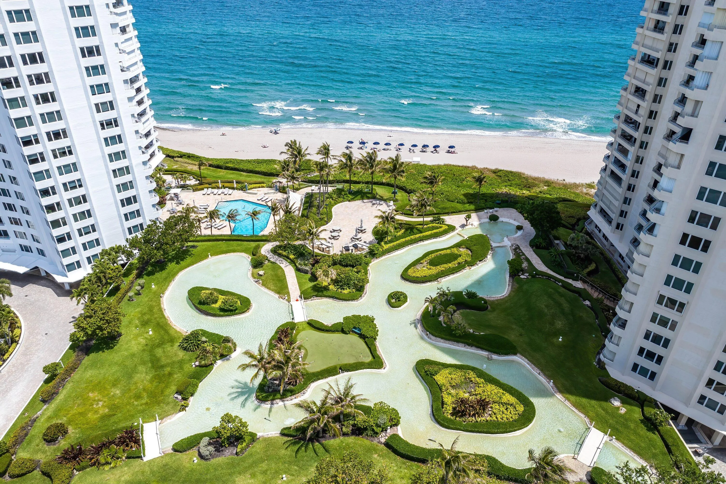 Expansive grounds featuring a meandering water feature, lush landscaping, a resort-style swimming pool, and direct beach access