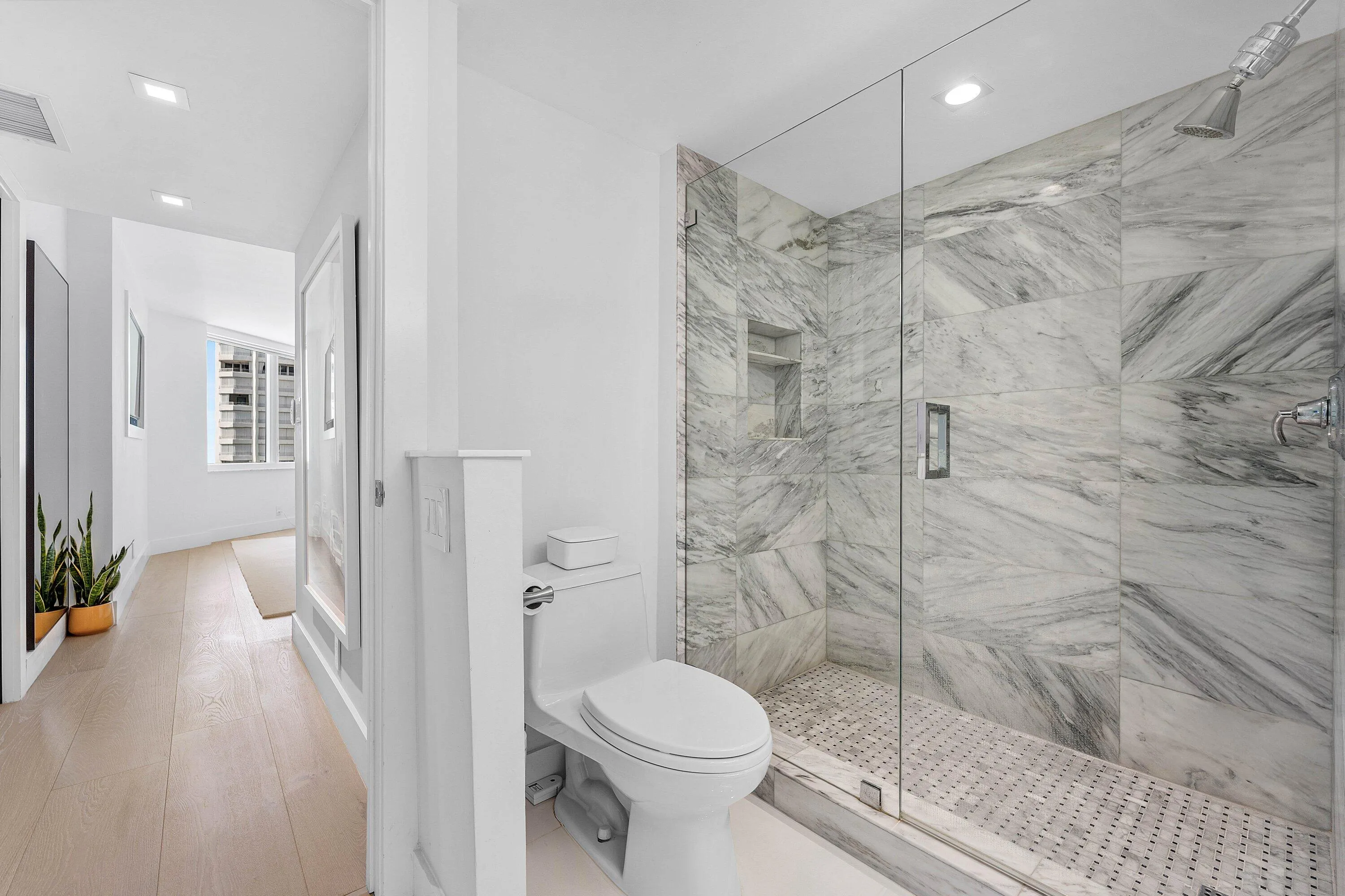 Glass-enclosed shower with full-height stone-finish wall tiling, recessed shower niche, and mosaic tile flooring
