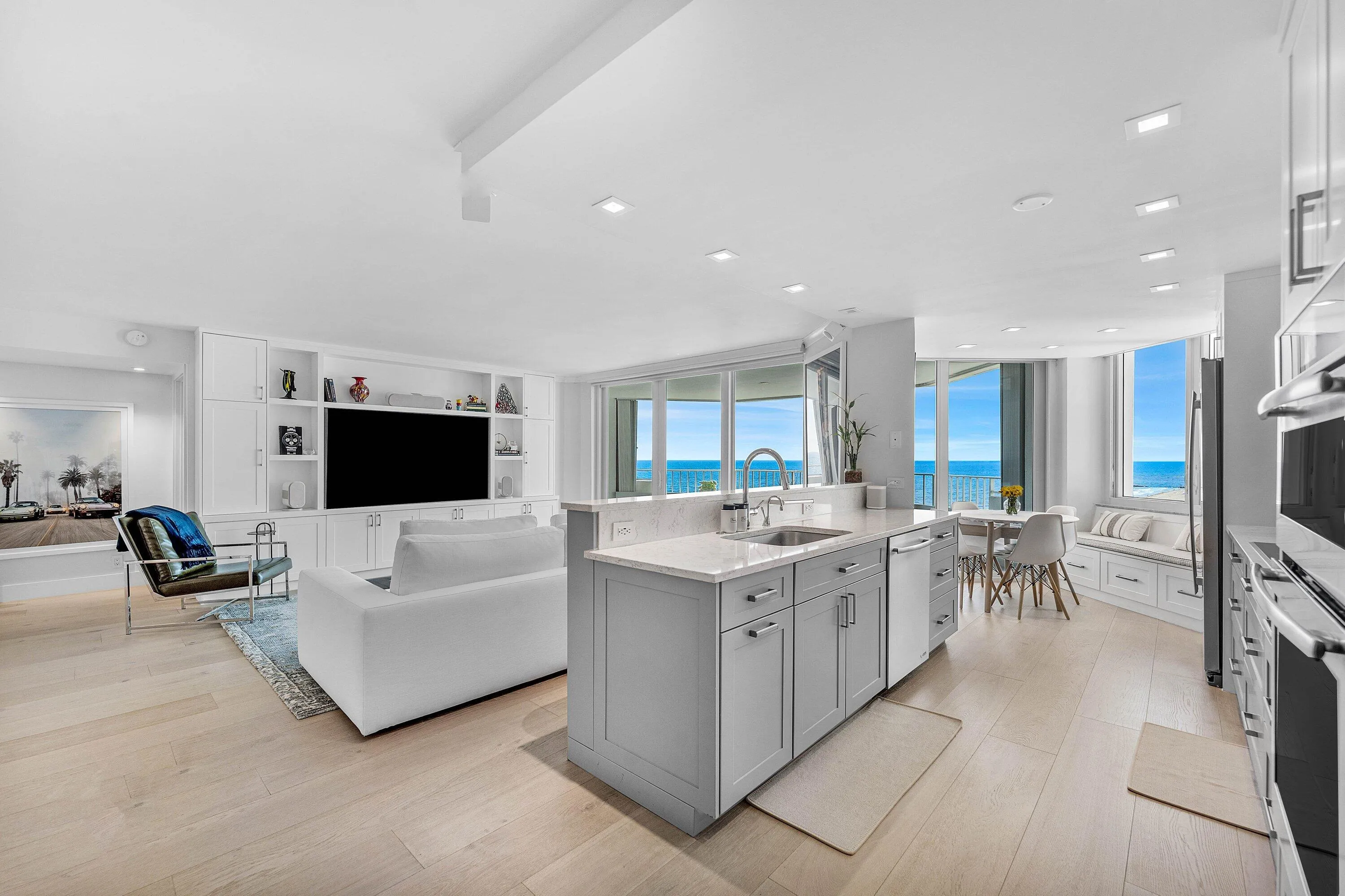 Open concept living area with wood-finish flooring, custom built-in entertainment center, kitchen island with sink, integrated appliances, and floor-to-ceiling windows