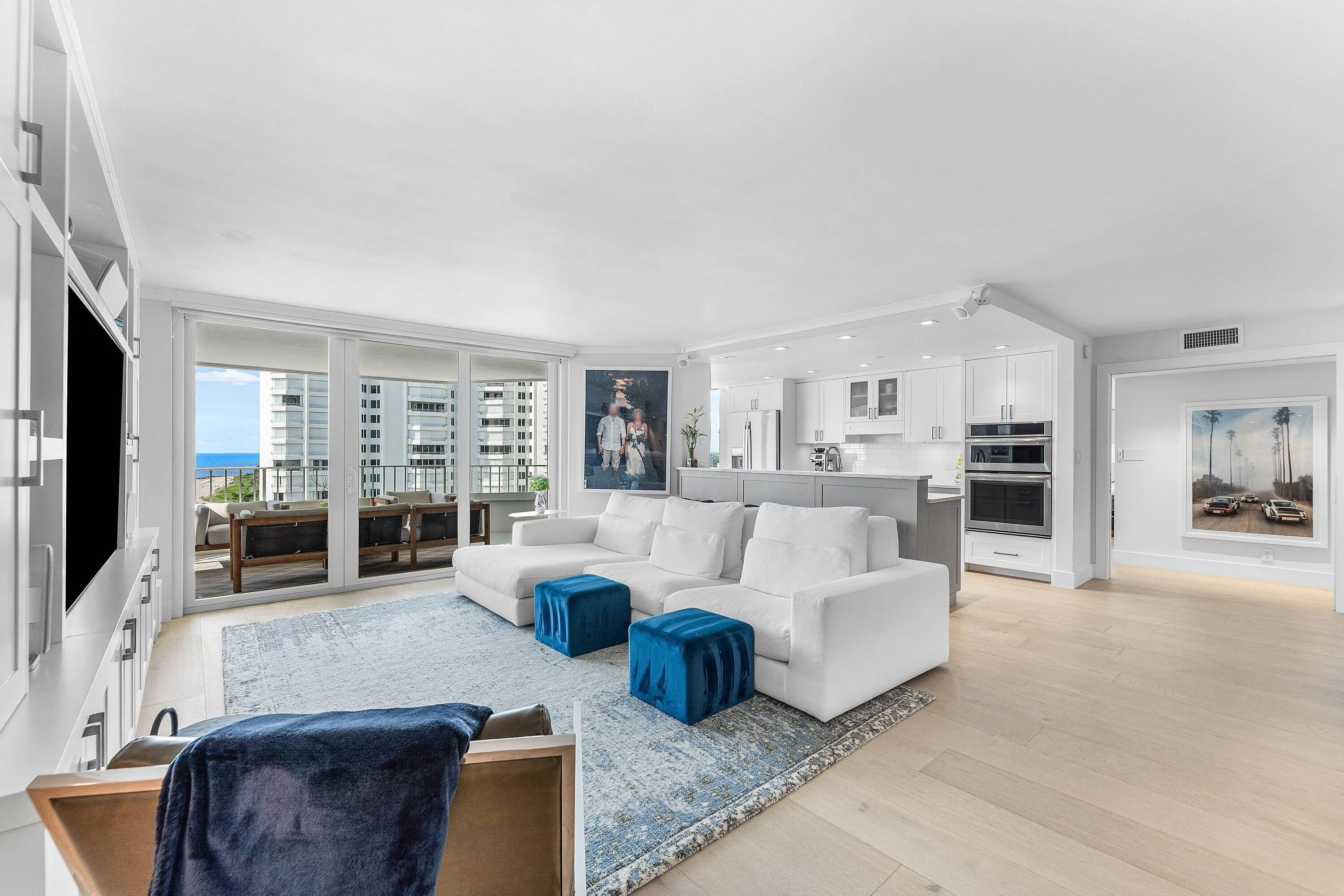 Open-concept living space featuring wood-finish flooring, built-in entertainment cabinetry, a kitchen with stainless steel appliances, and a balcony with an ocean backdrop
