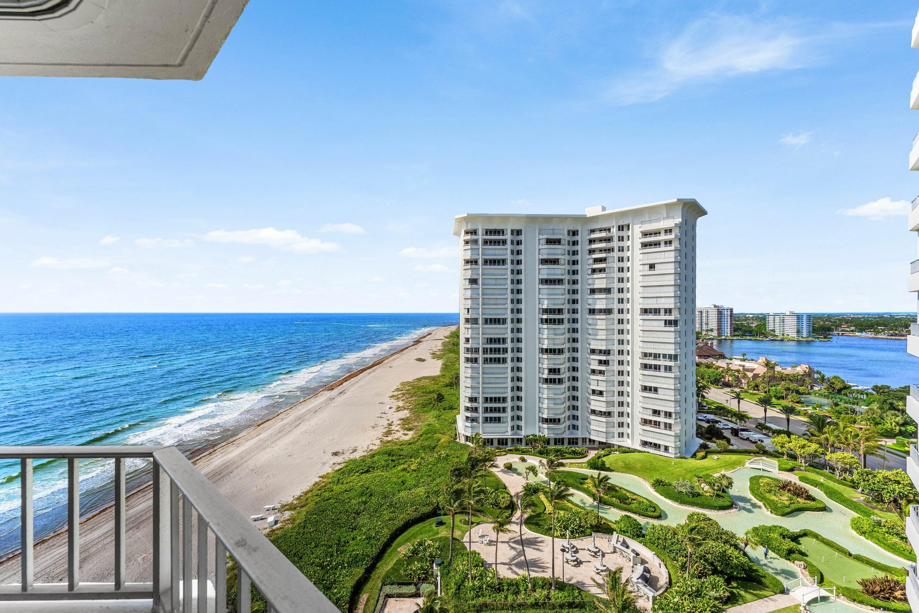 Expansive oceanfront balcony with metal railing, offering direct beach access, a landscaped putting green, and waterway frontage