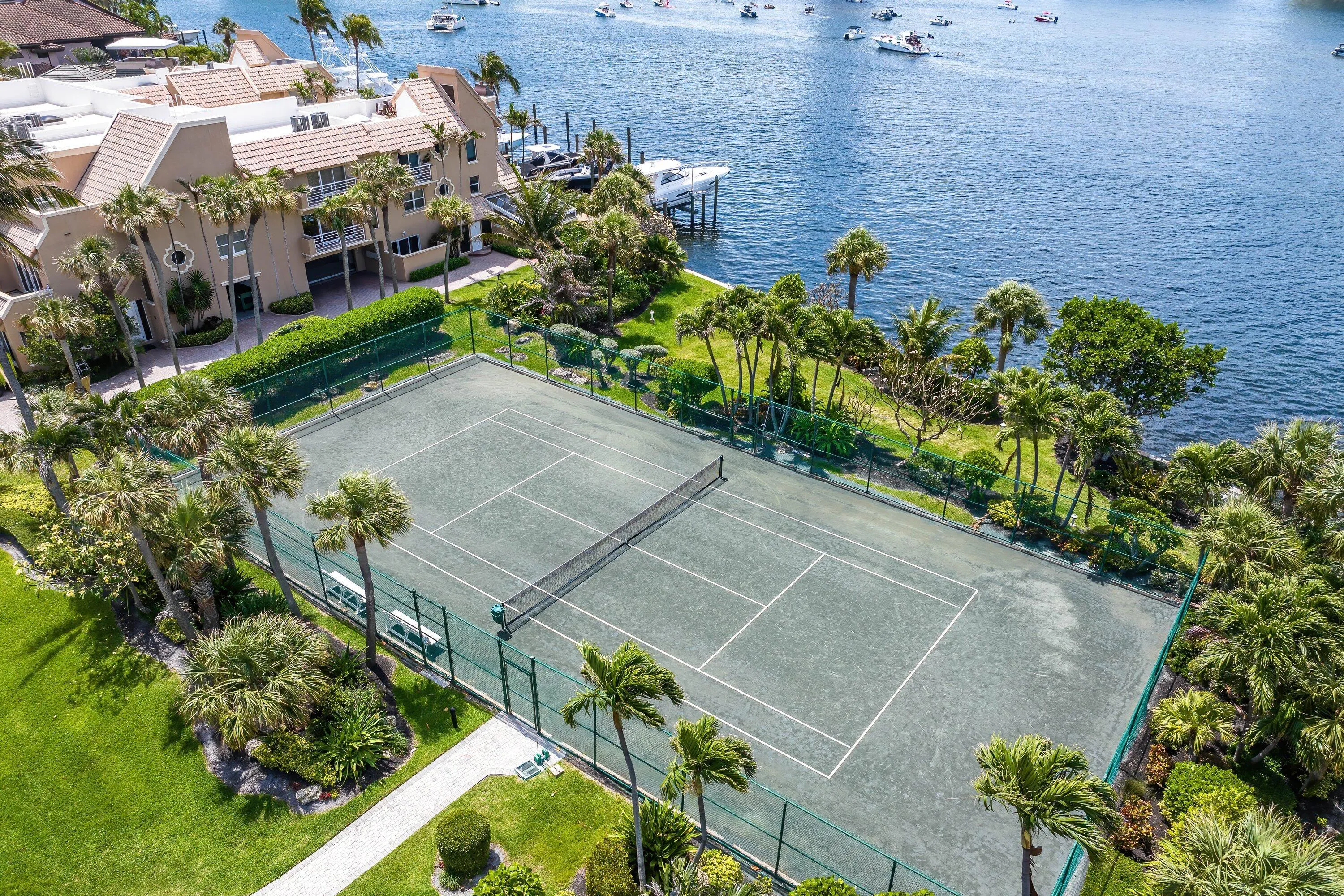 Waterfront property with private tennis court, manicured landscaping, and mature palm trees