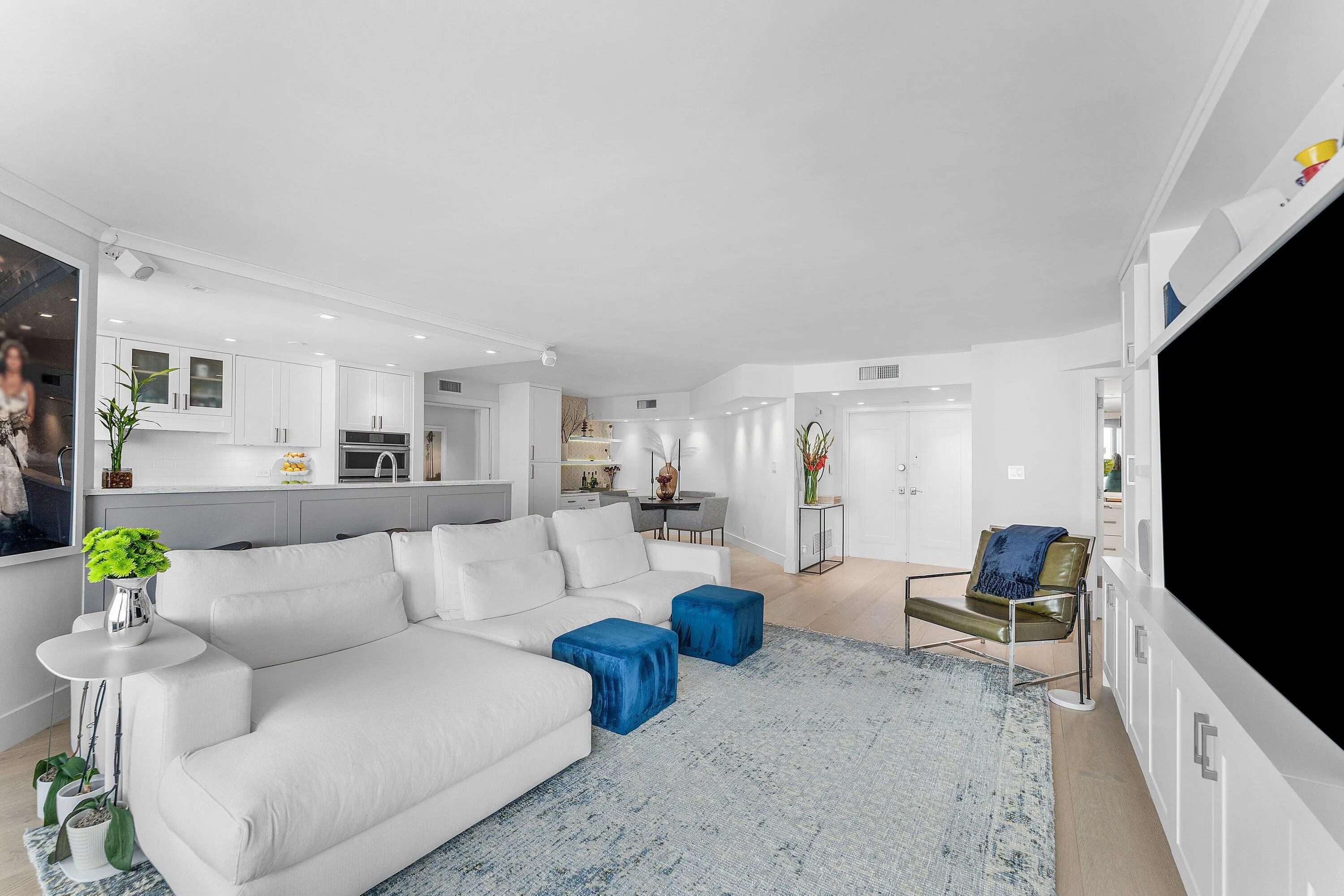 Open-concept living area featuring light wood-finish flooring, recessed lighting, and a kitchen with white cabinetry and an undermount sink