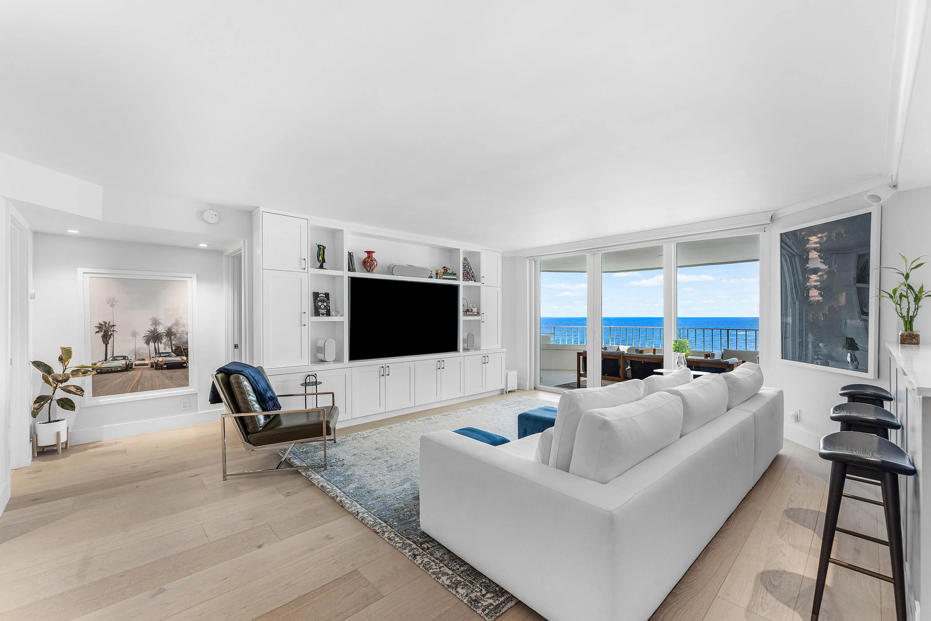 Expansive sliding glass doors, built-in entertainment center with white cabinetry, light wood-finish flooring, recessed lighting, and balcony with water scenery