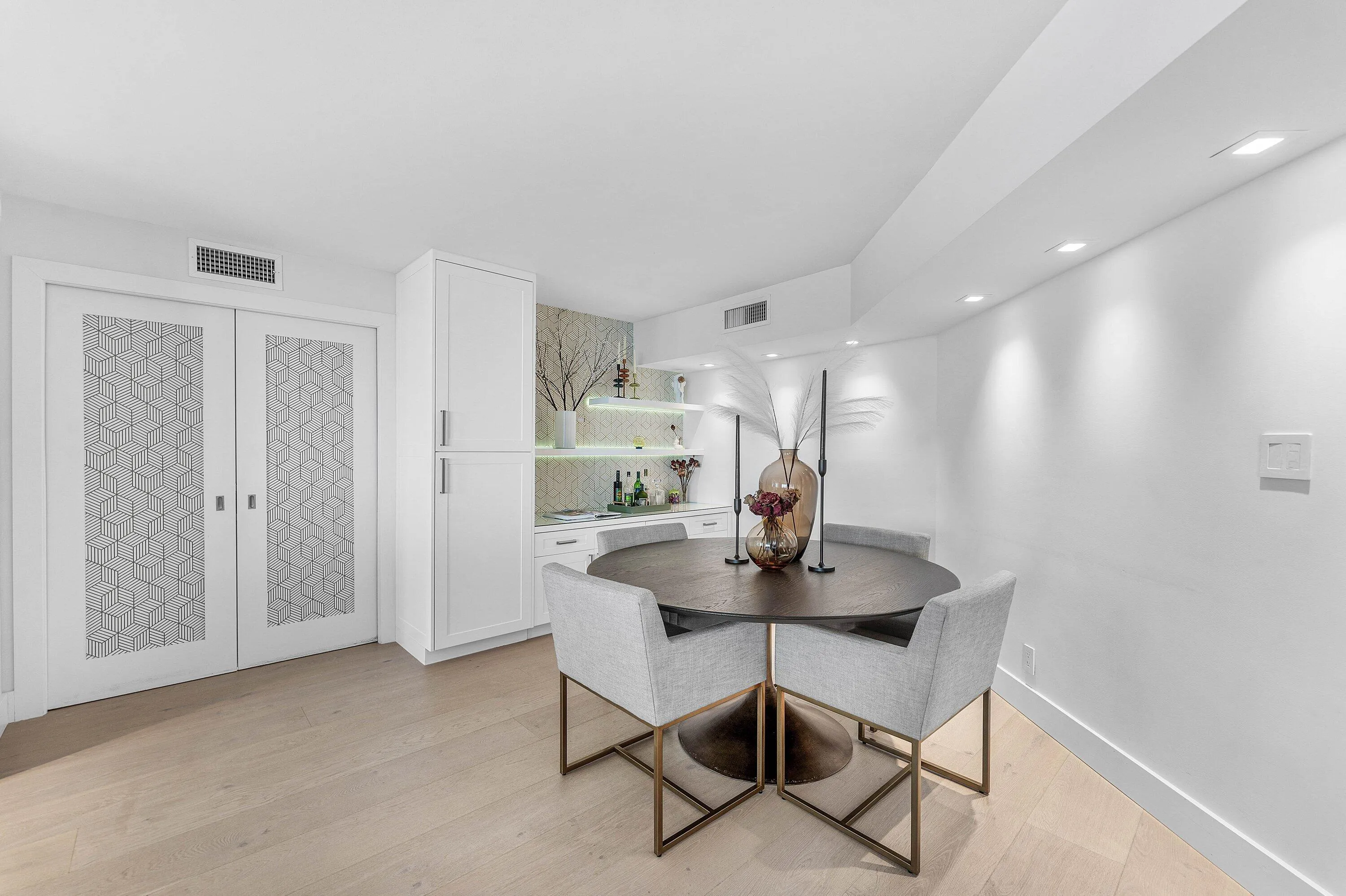 Light wood-finish flooring, built-in wet bar with shelving, white cabinetry, recessed ceiling lighting, and sliding doors with patterned glass inserts