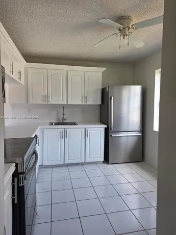 Kitchen featuring white cabinetry, stainless steel appliances, a corner sink, white tile flooring, and a ceiling fan