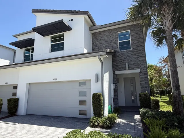 Modern exterior featuring a stone accent wall, decorative window awnings, an integrated two-car garage, and a paver driveway