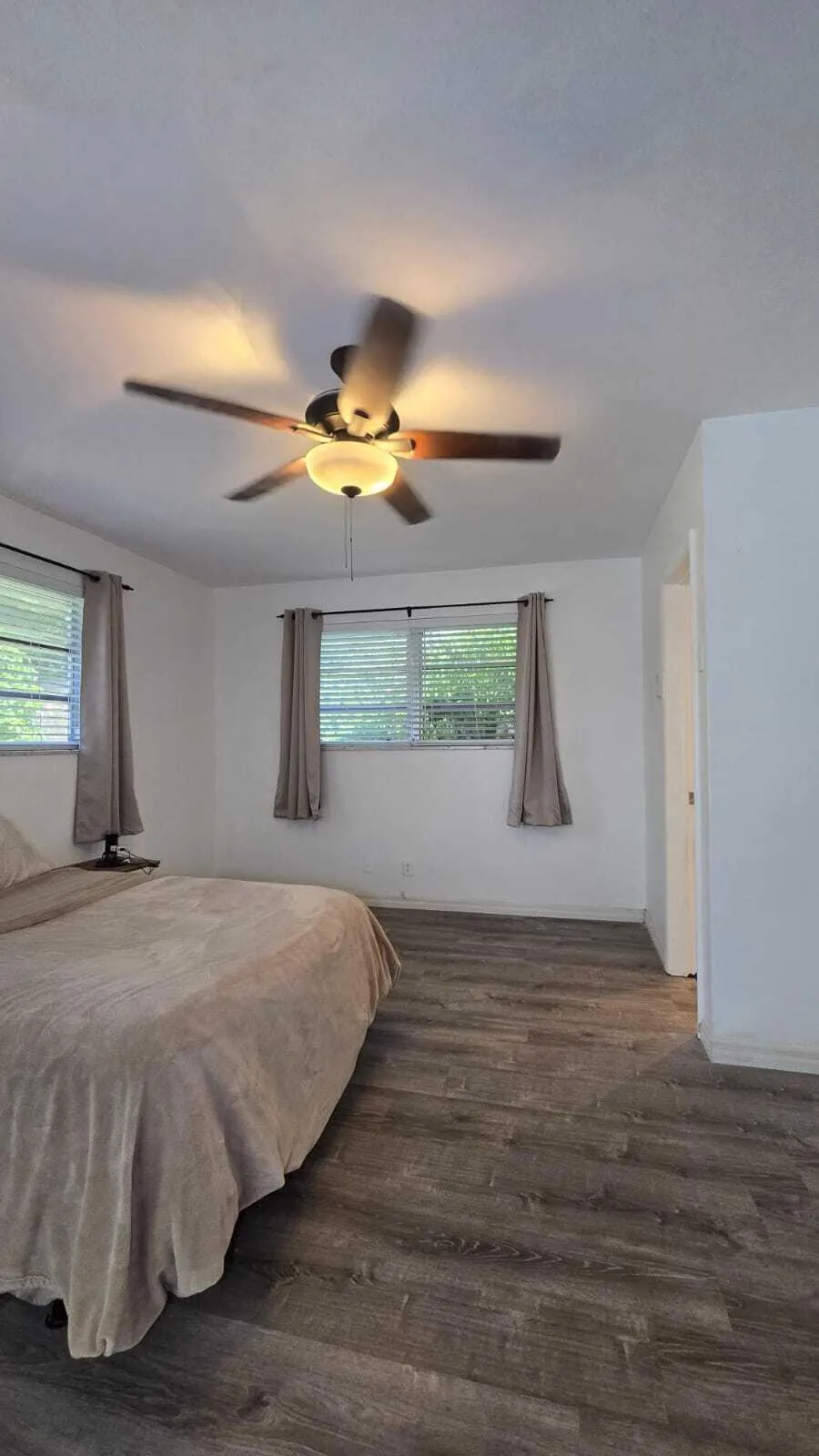 Wood-finish flooring throughout, two windows with blinds, and a ceiling fan with integrated lighting