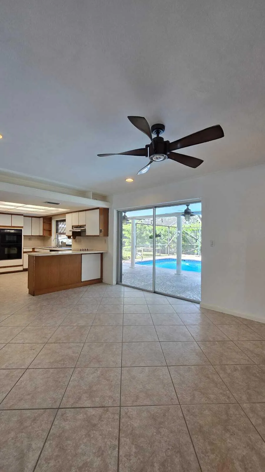 Tiled flooring, ceiling fan, kitchen with two-tone cabinetry, kitchen island, and sliding glass doors opening to a screened pool area